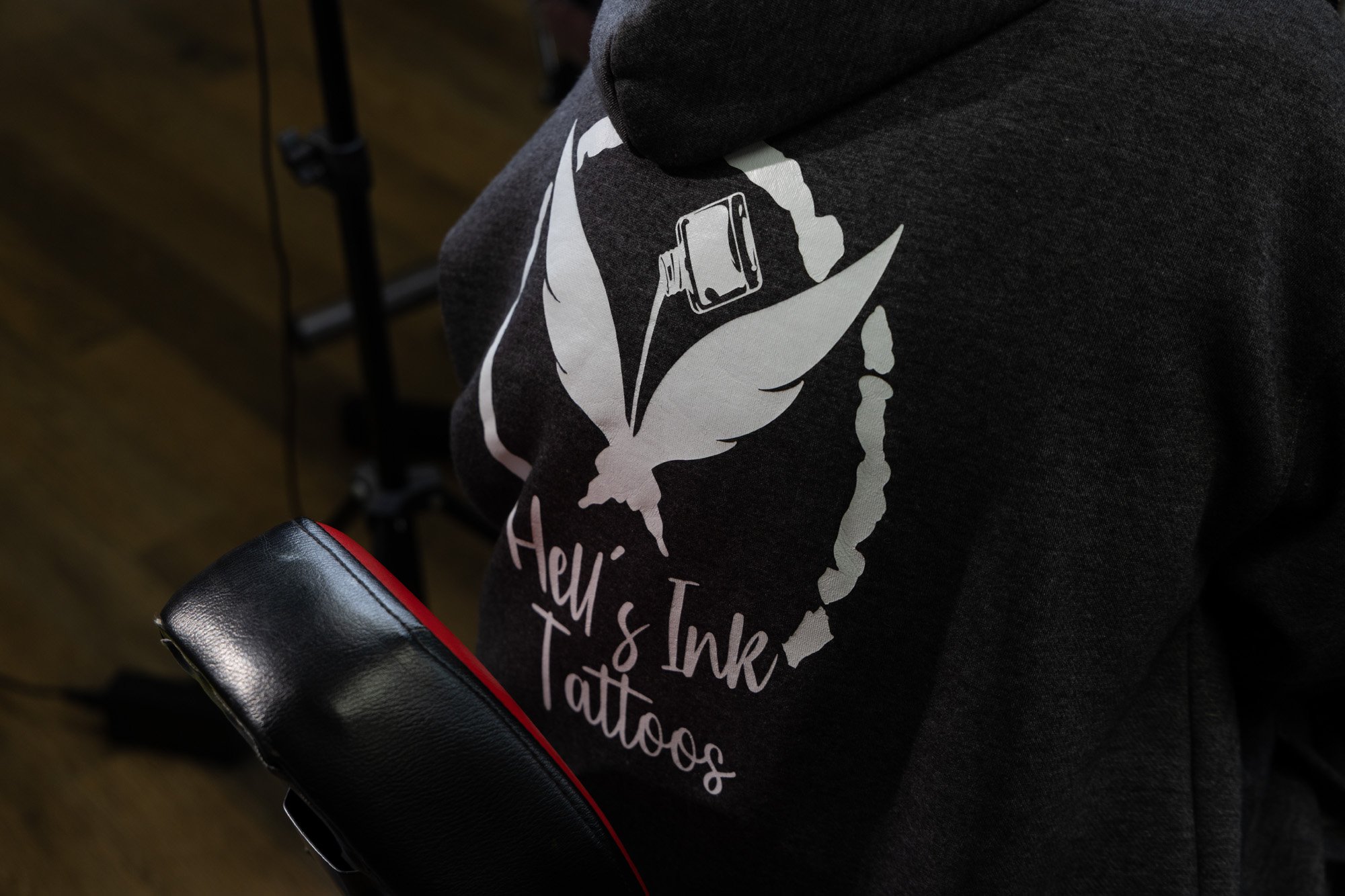 Close-up of a person wearing a black hoodie with white text and graphics, sitting on a black chair with a red edge.