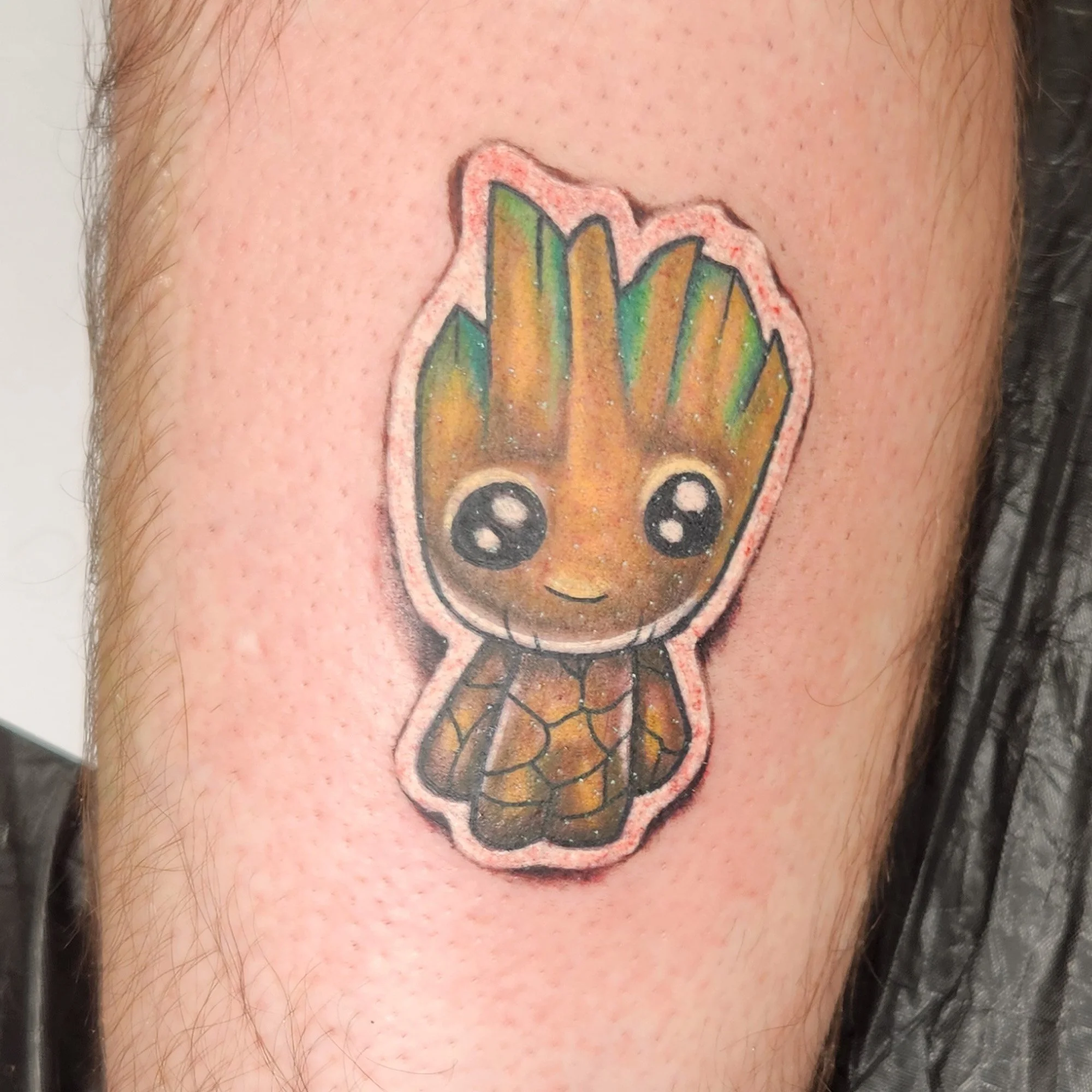 Close-up of a colorful tattoo of a cartoon-style baby groot