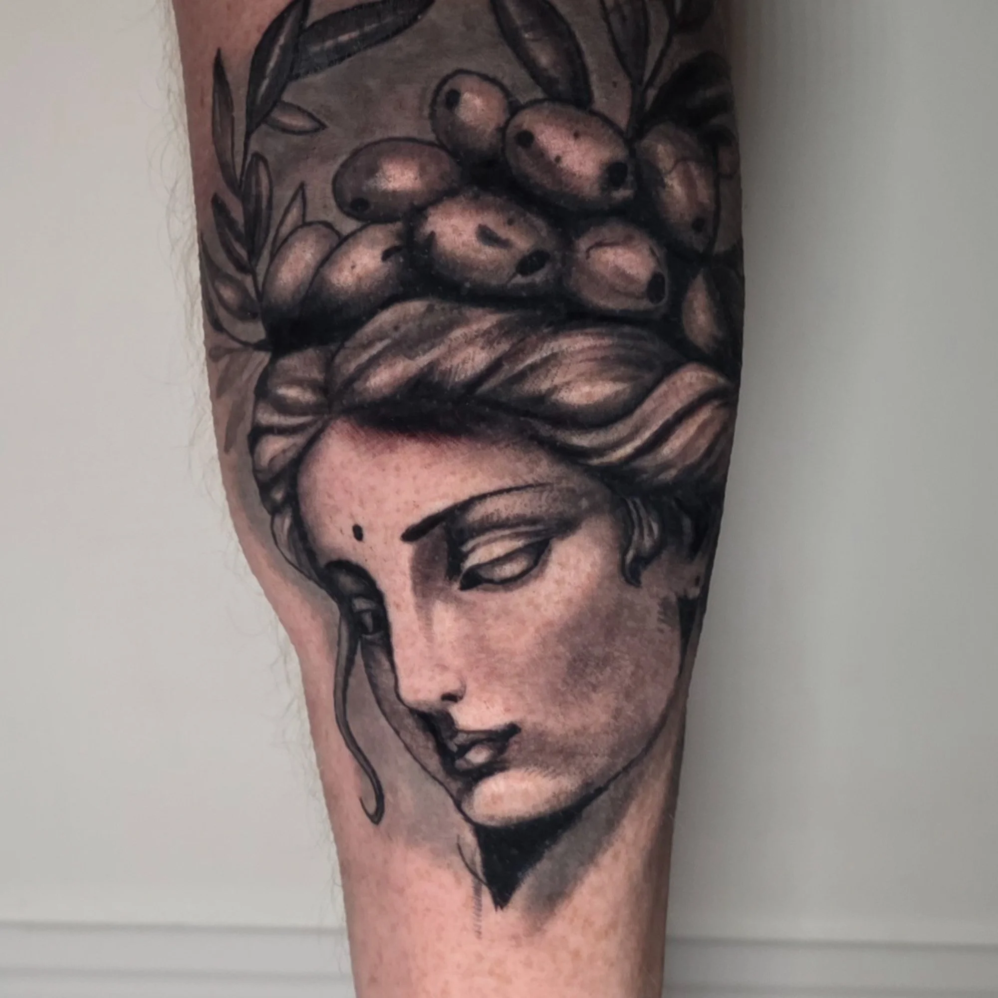 Close-up of a tattoo depicting a woman's face surrounded by leaves, with long hair and closed eyes.