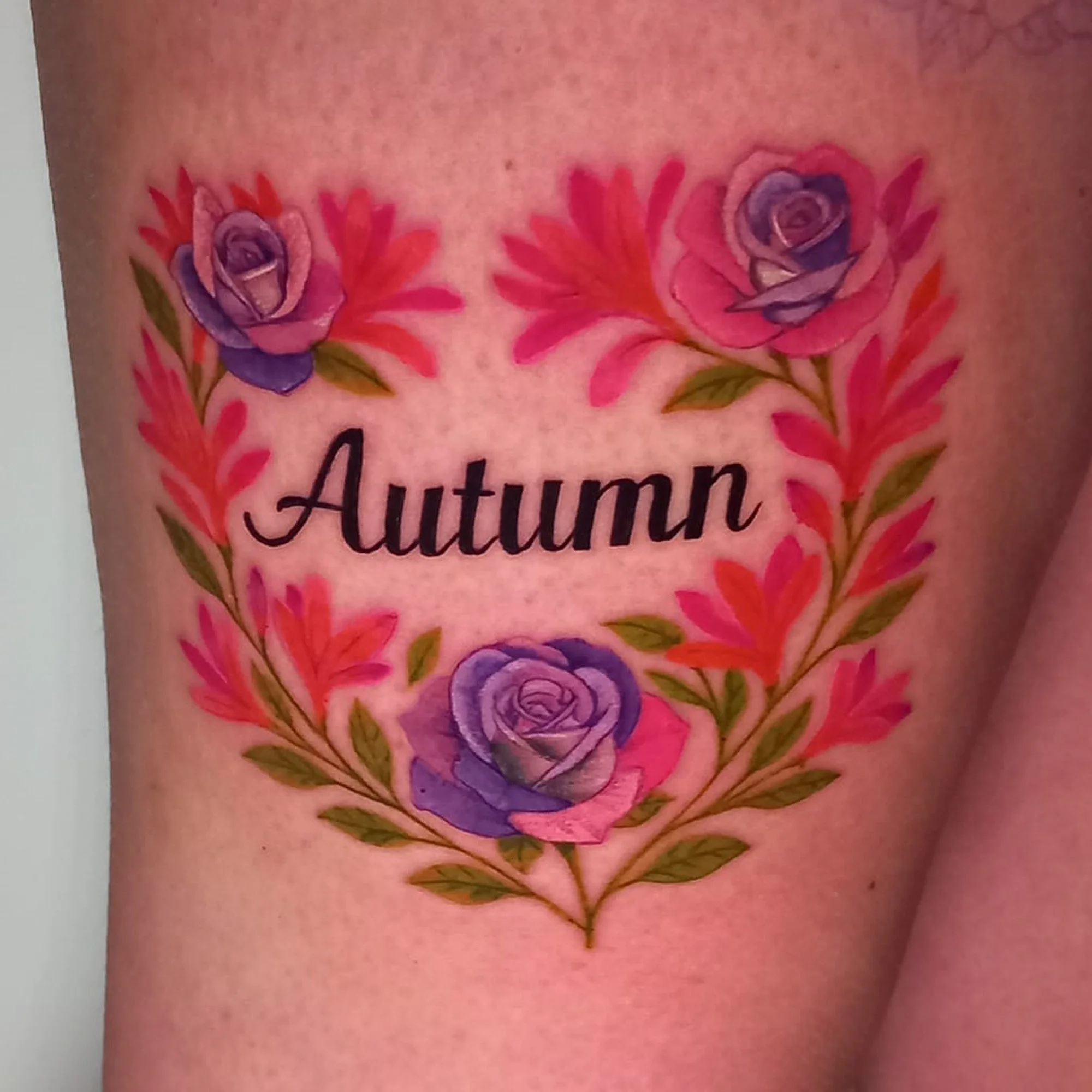 Colorful tattoo of purple and pink roses with green leaves on person’s skin.
