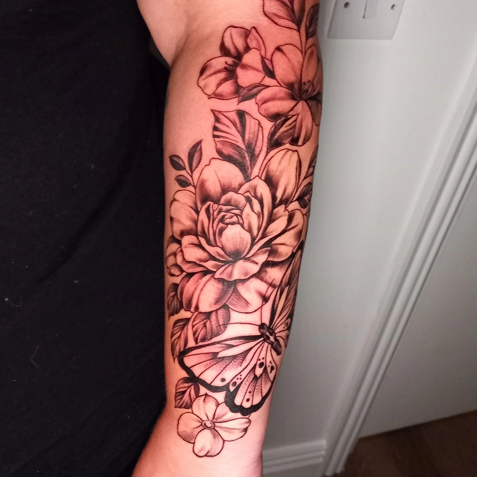 A tattoo of pink and black flowers and butterfly on a person's arm.
