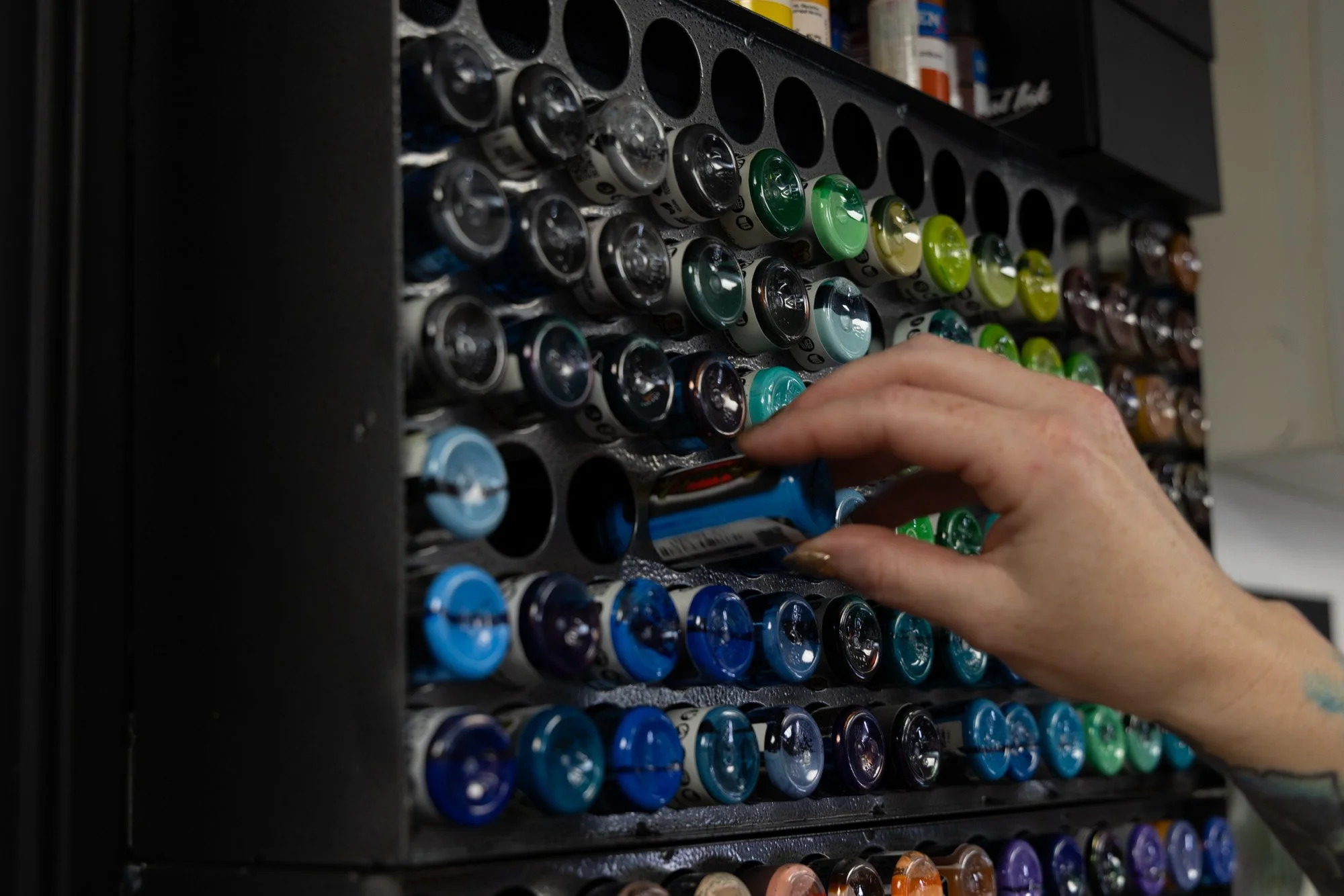 Person's hand reaching into a vending machine filled with colorful cans of soda.
