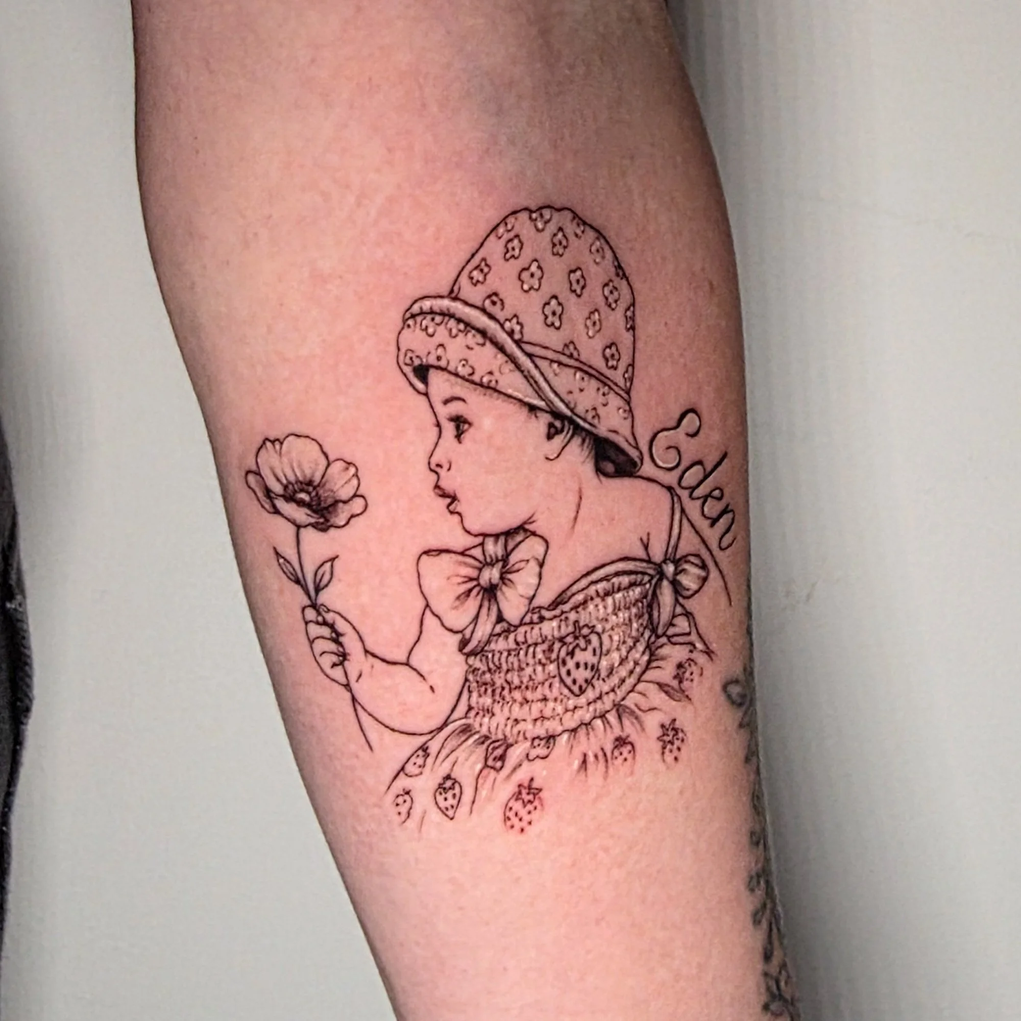 A tattoo of a woman's face wearing a hat with a floral pattern and the words 'Explore the world' on a person's upper arm.