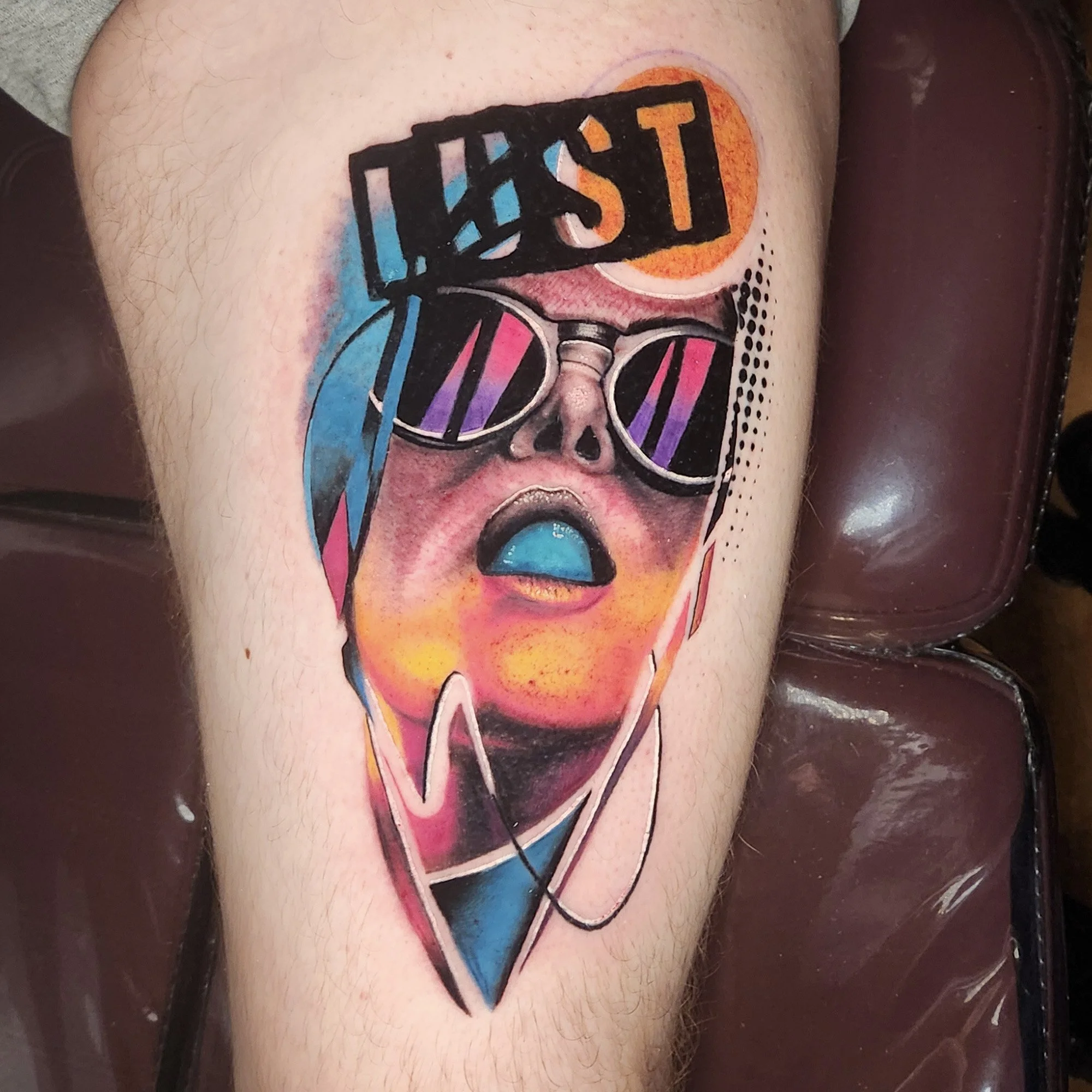Tattoo of a woman's face wearing sunglasses with rainbow-colored lenses, outlined in black, on upper arm.