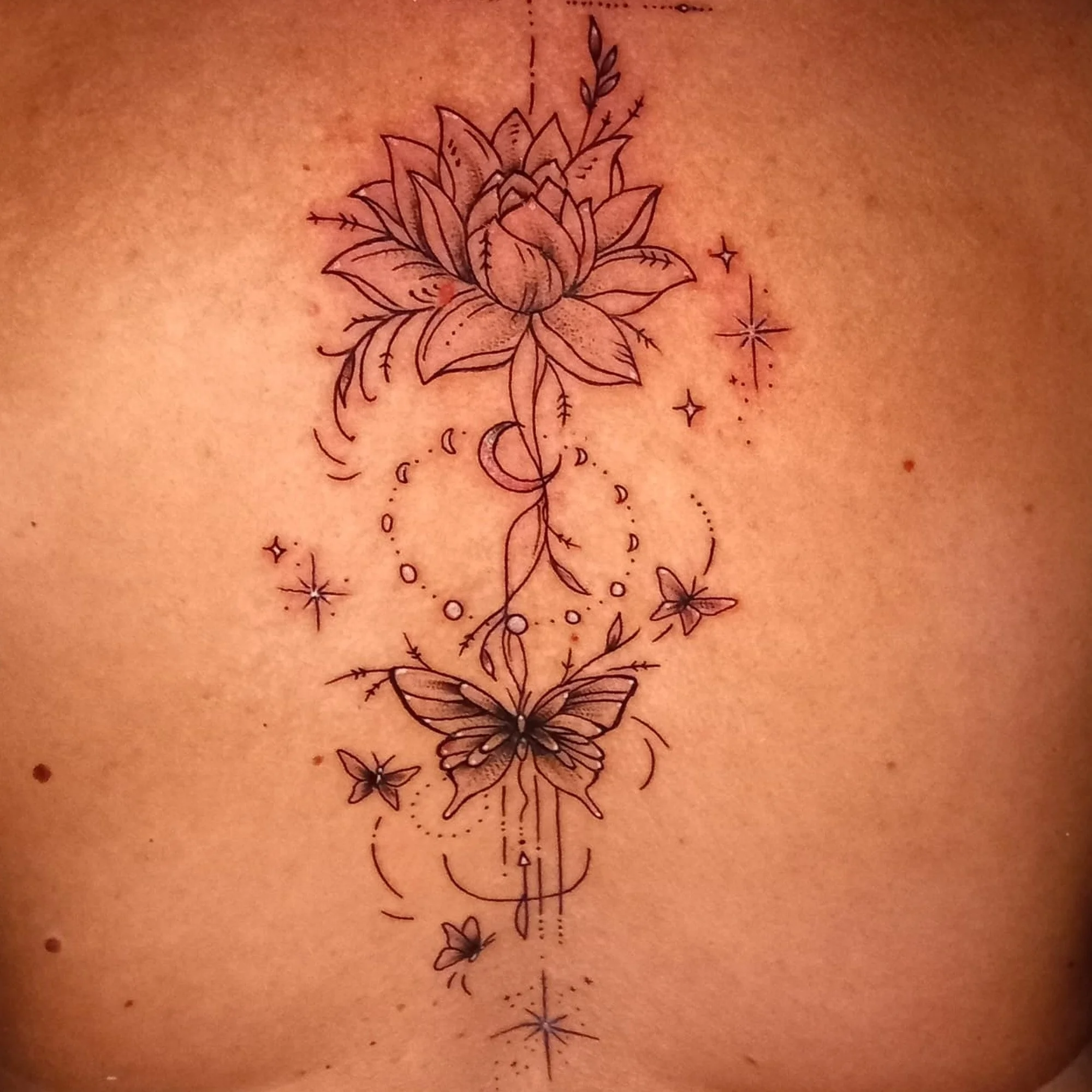 A black outline tattoo of a rose flower with leaves and stems, accompanied by small decorative stars and crescent moons, on skin.