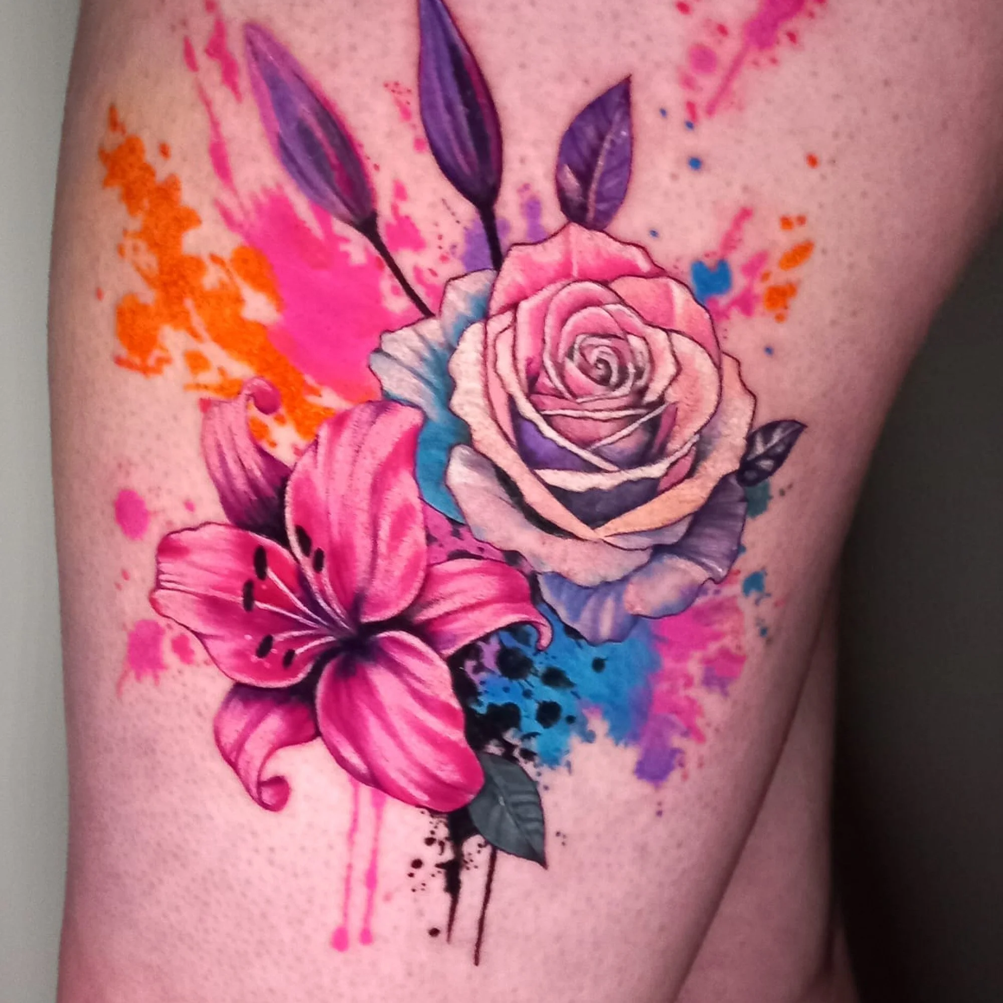 A colorful tattoo featuring a large pink rose, purple leaves, orange splashes, and black ink details on a person's skin.