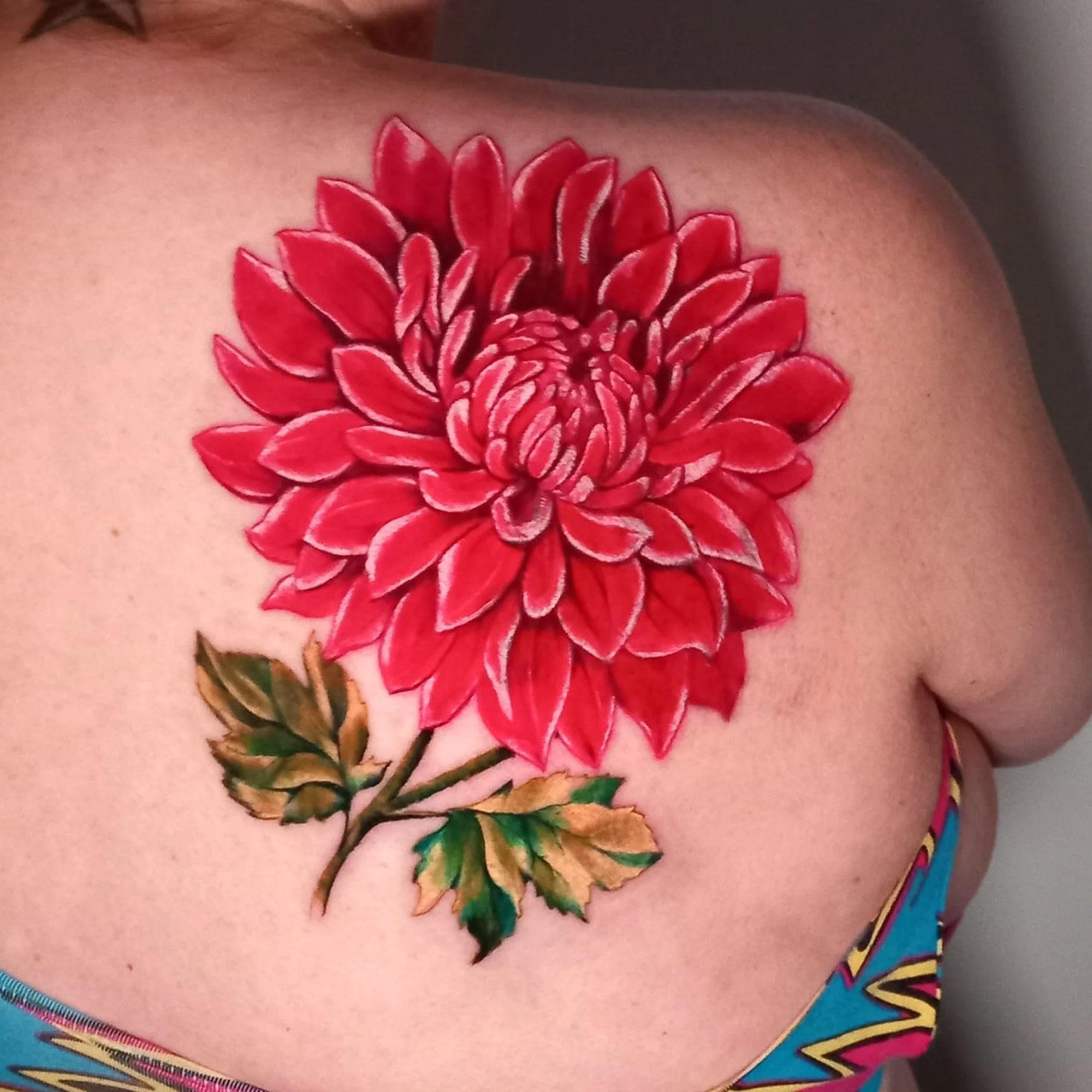A vibrant tattoo of a large red flower with green leaves on a person's upper chest.