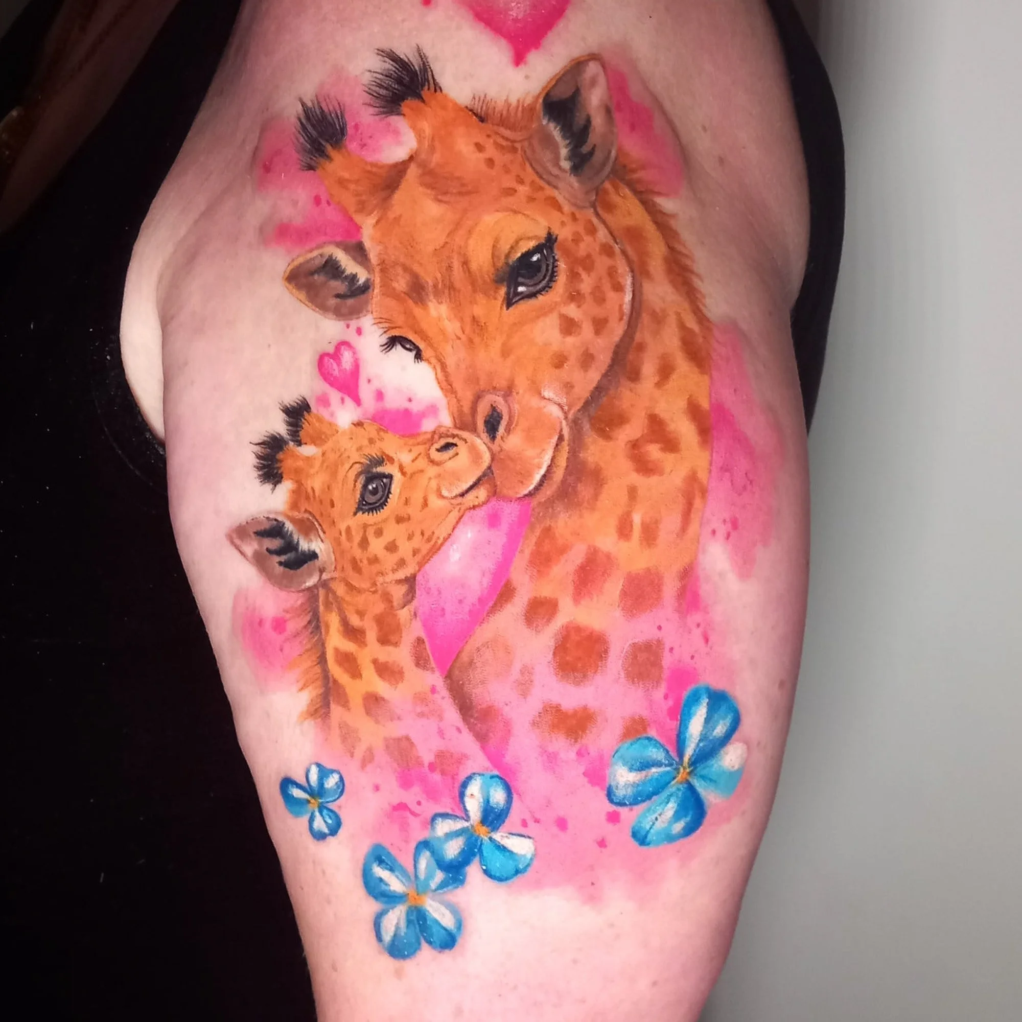 Tatoo of two baby giraffes with flowers, and a pink splash background.