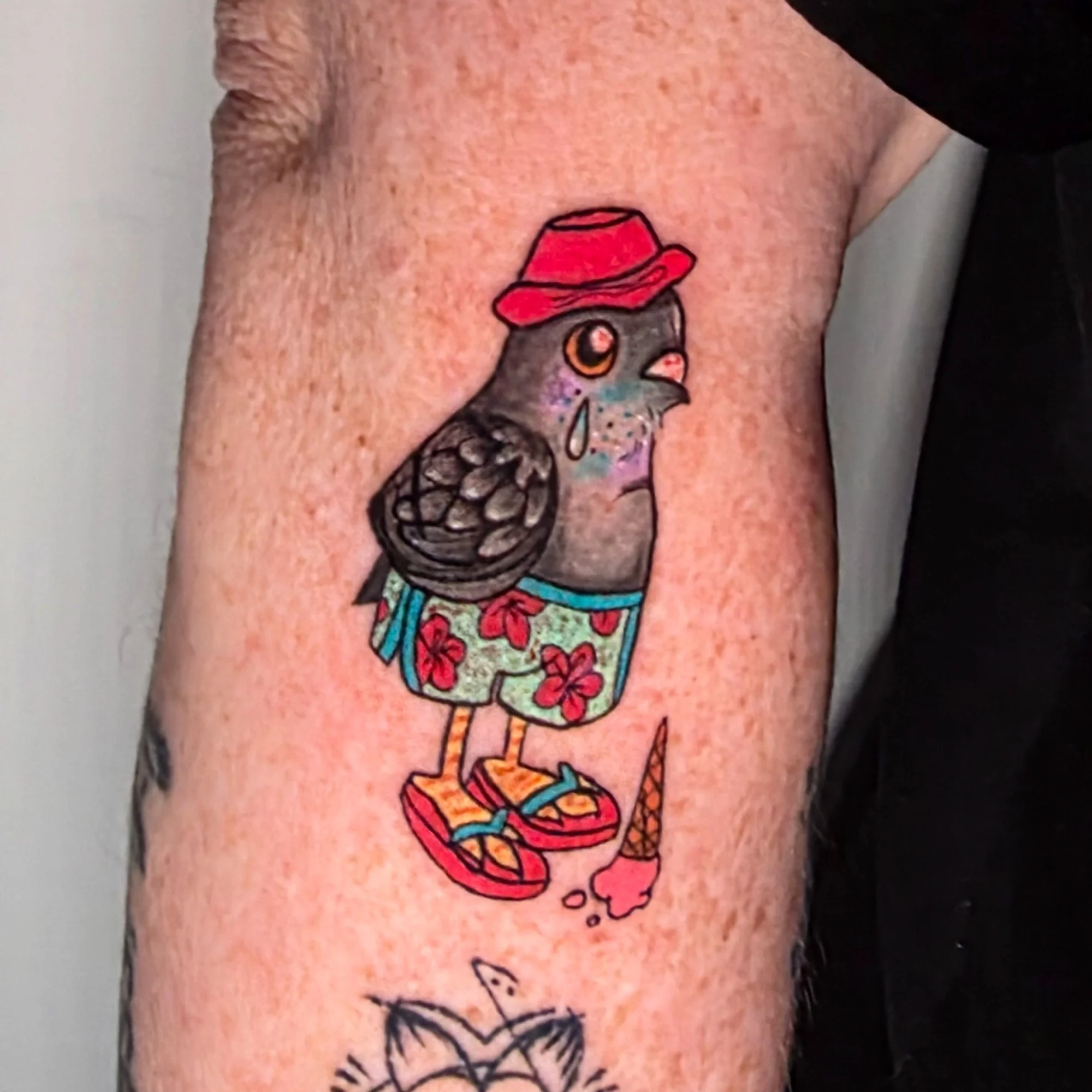 A colorful tattoo of a pigeon wearing a red hat and a floral dress.