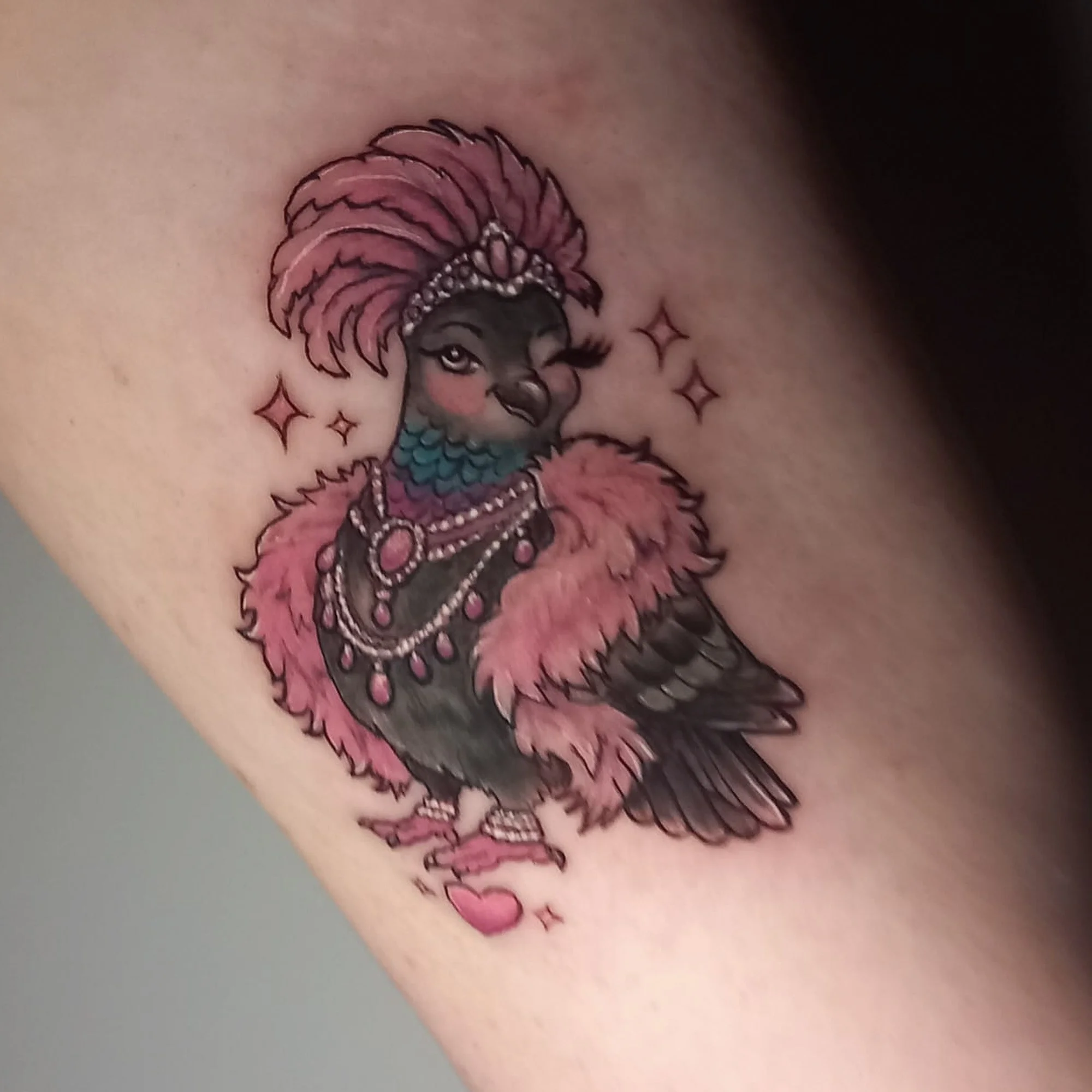 Colourful tattoo of a pigeon with a pink mane, wearing pearl jewellery, on a person's skin.