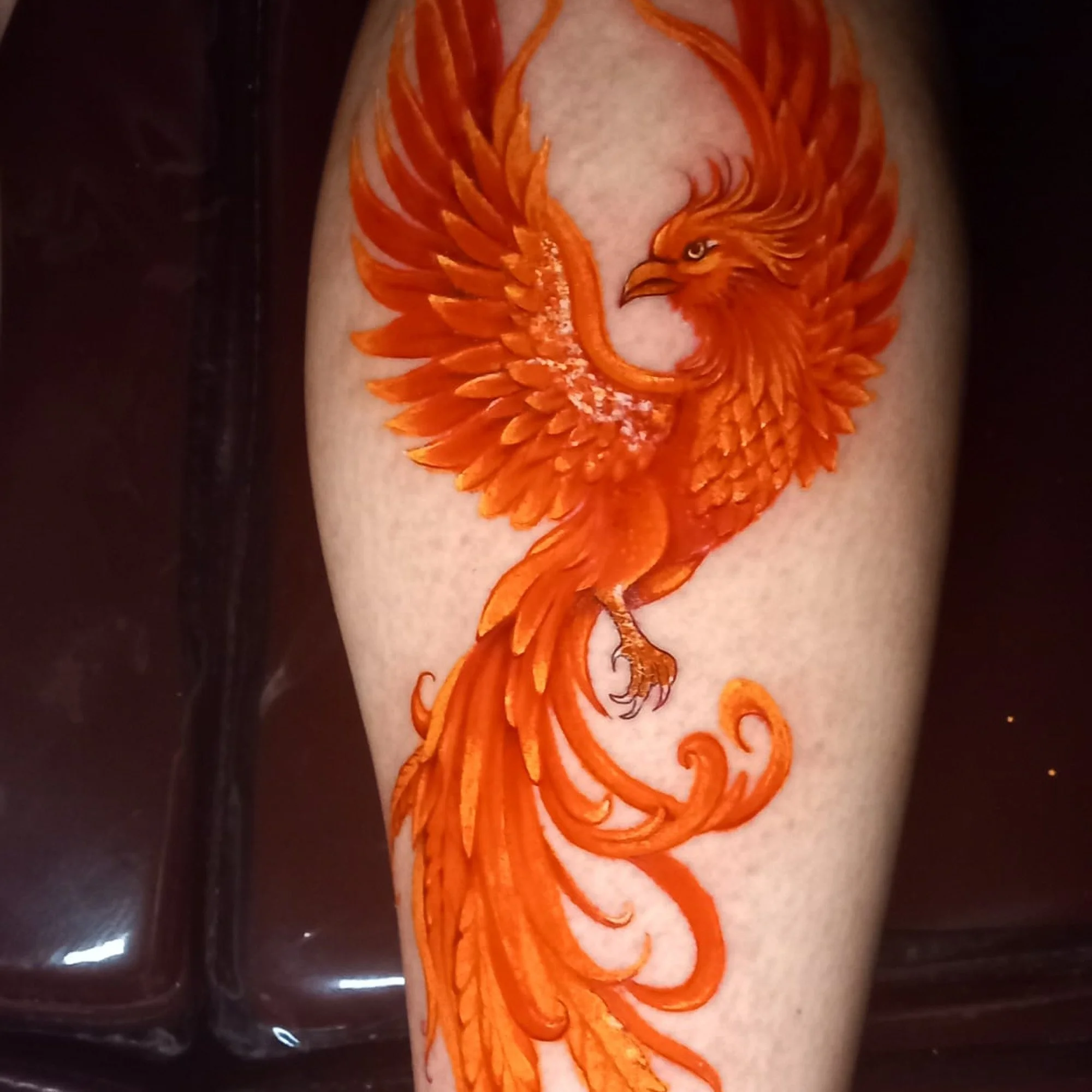 A detailed orange and white tattoo of a phoenix on a person's arm.