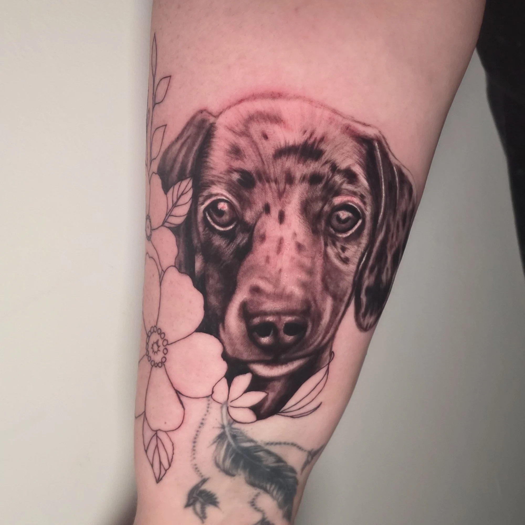 Tattoo of a lion's face on a person's arm, with some floral and leaf designs around it.