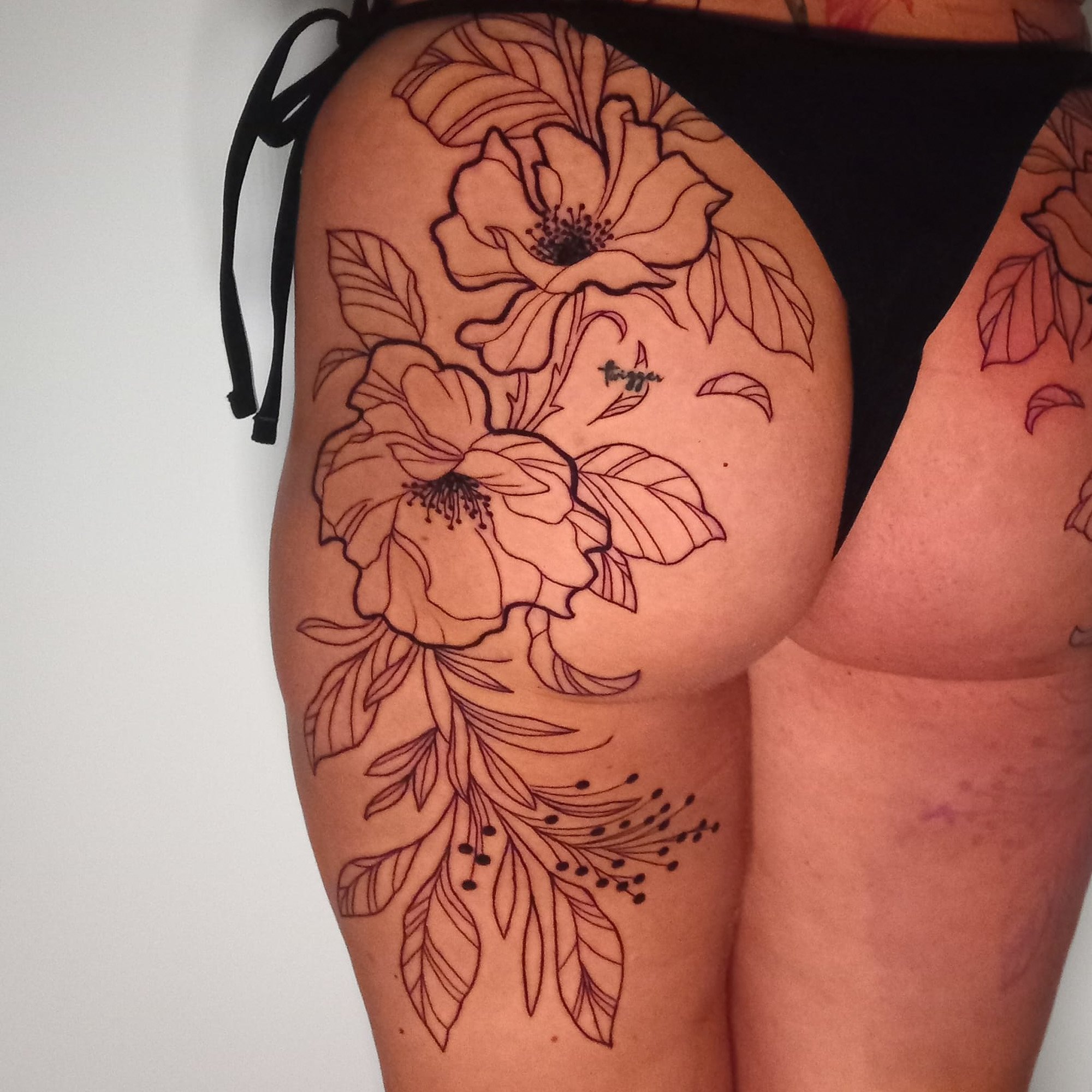 A floral tattoo of outline style flowers and leaves on a person's upper arm.