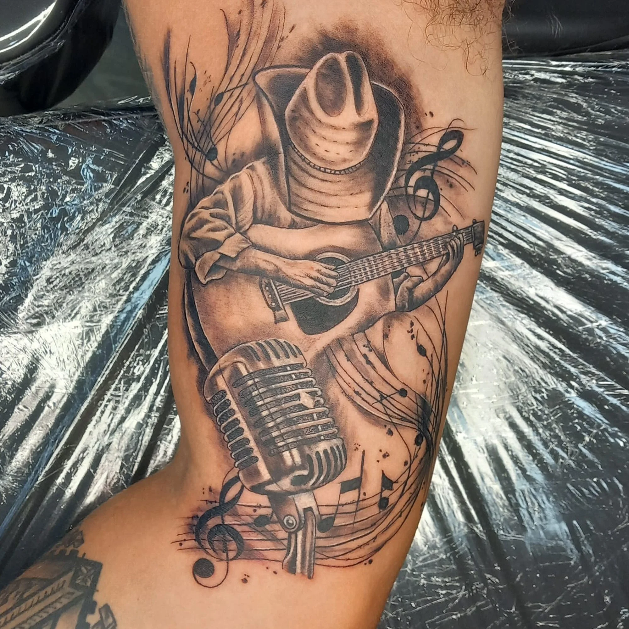 Tattoo of a smiling cowboy wearing a hat and playing an acoustic guitar on a person's arm.
