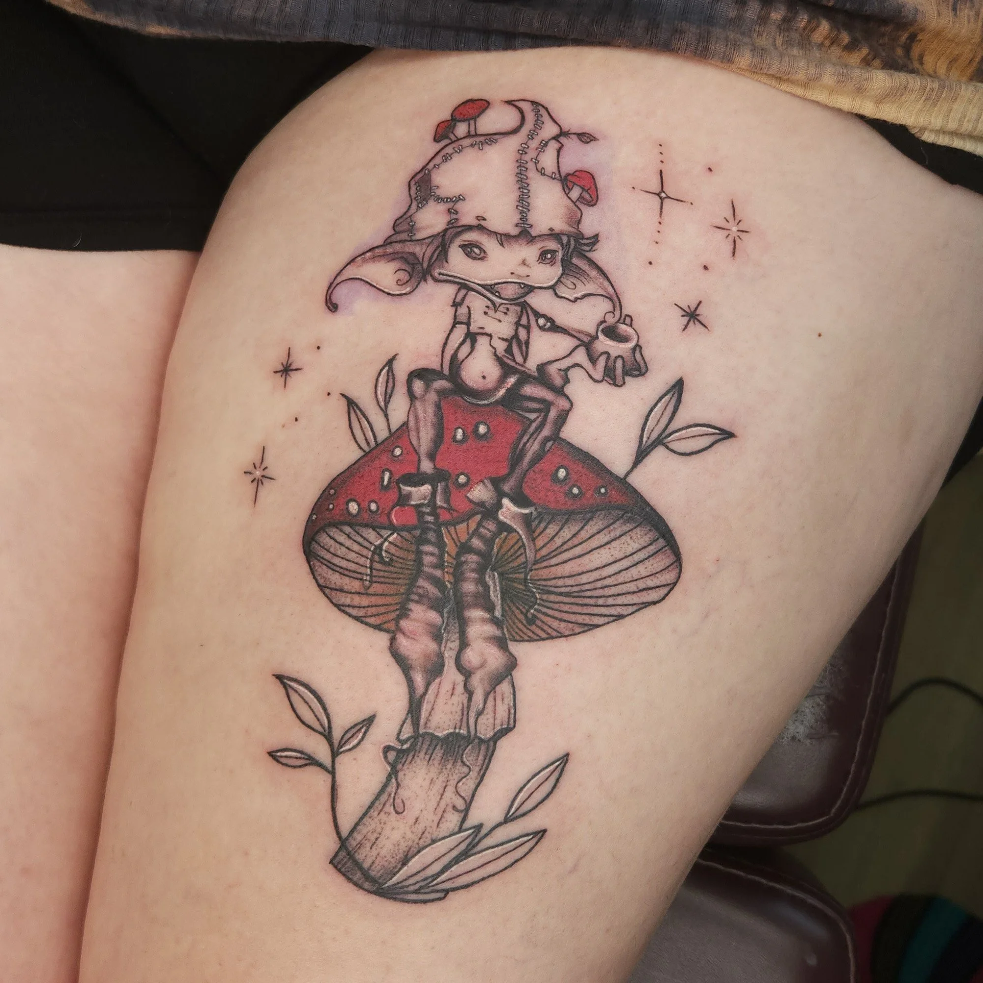 Tattoo of a creature sat on a red mushroom.
