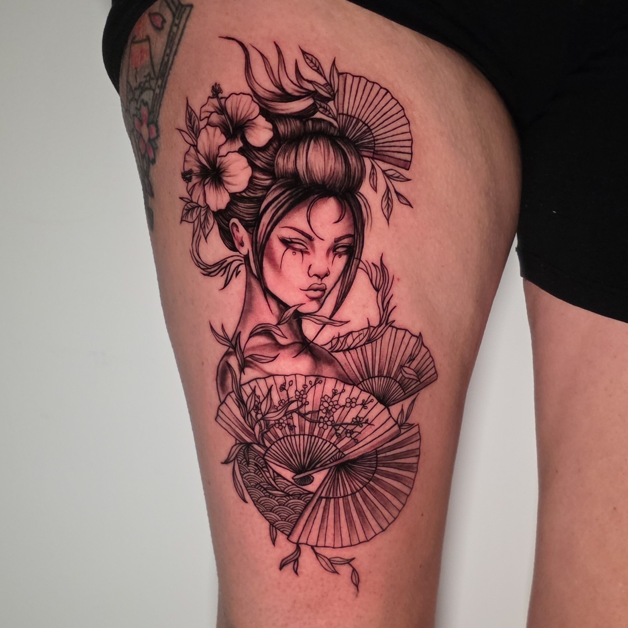 Line art tattoo of a woman with flowers, leaves, and Japanese fans on upper arm.