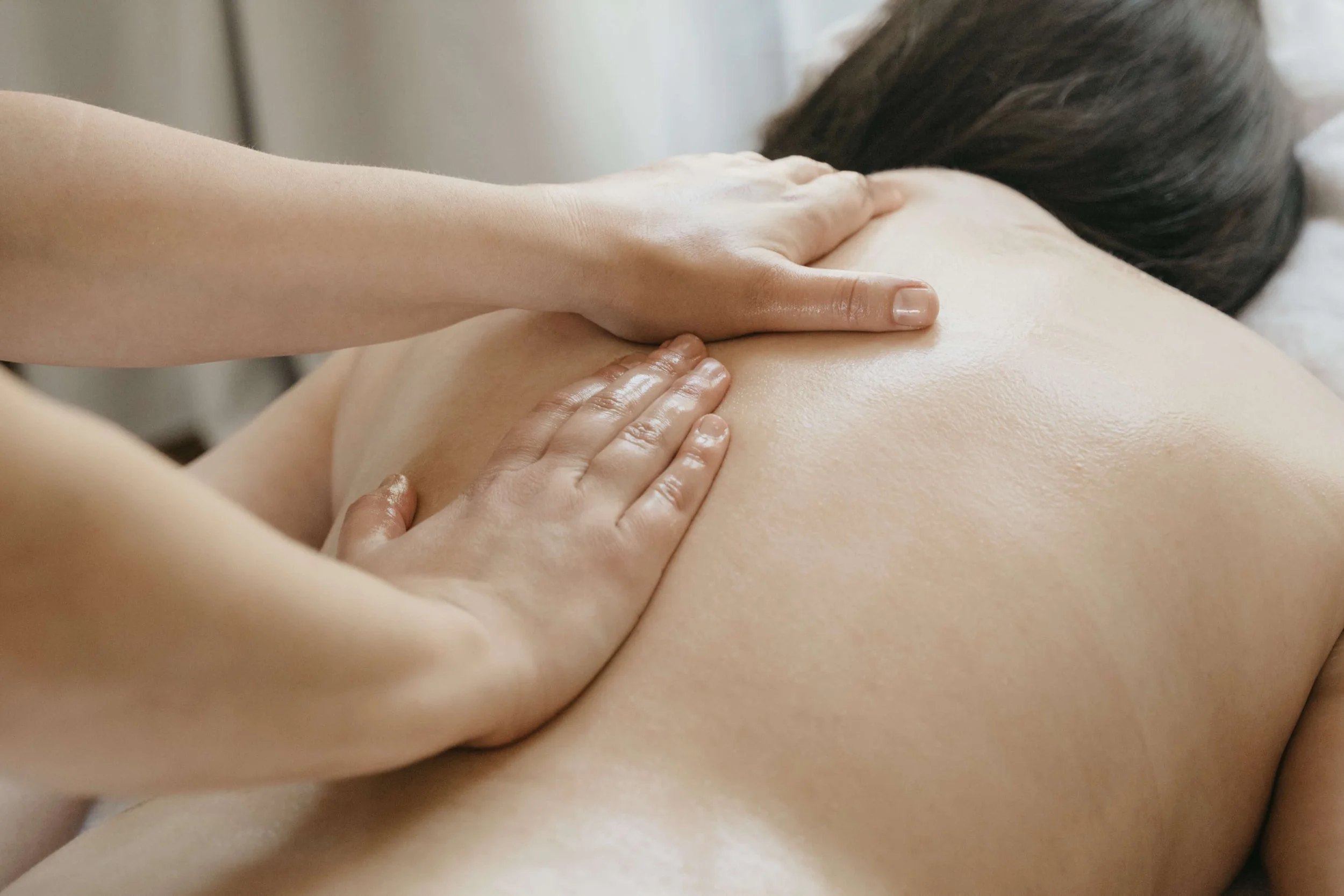 Une personne reçoit un massage avec de l'huile chaude sur le dos, la vue se concentre sur ses épaules et les paravertébraux.