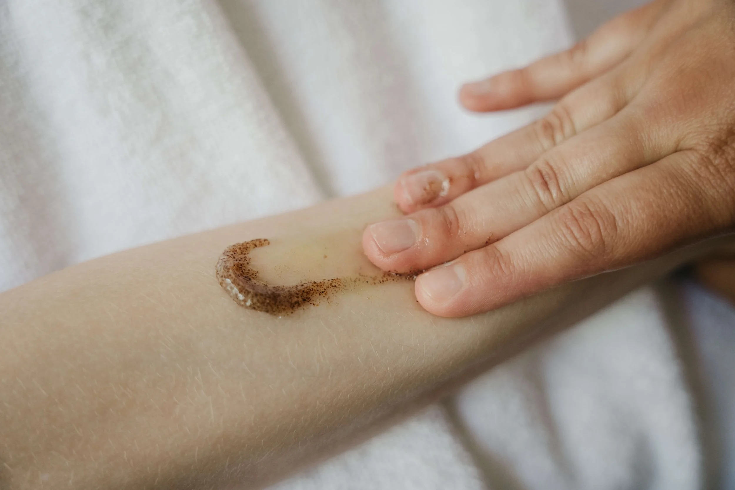 Une main applique en douceur un gommage corporel biologique sur la peau.