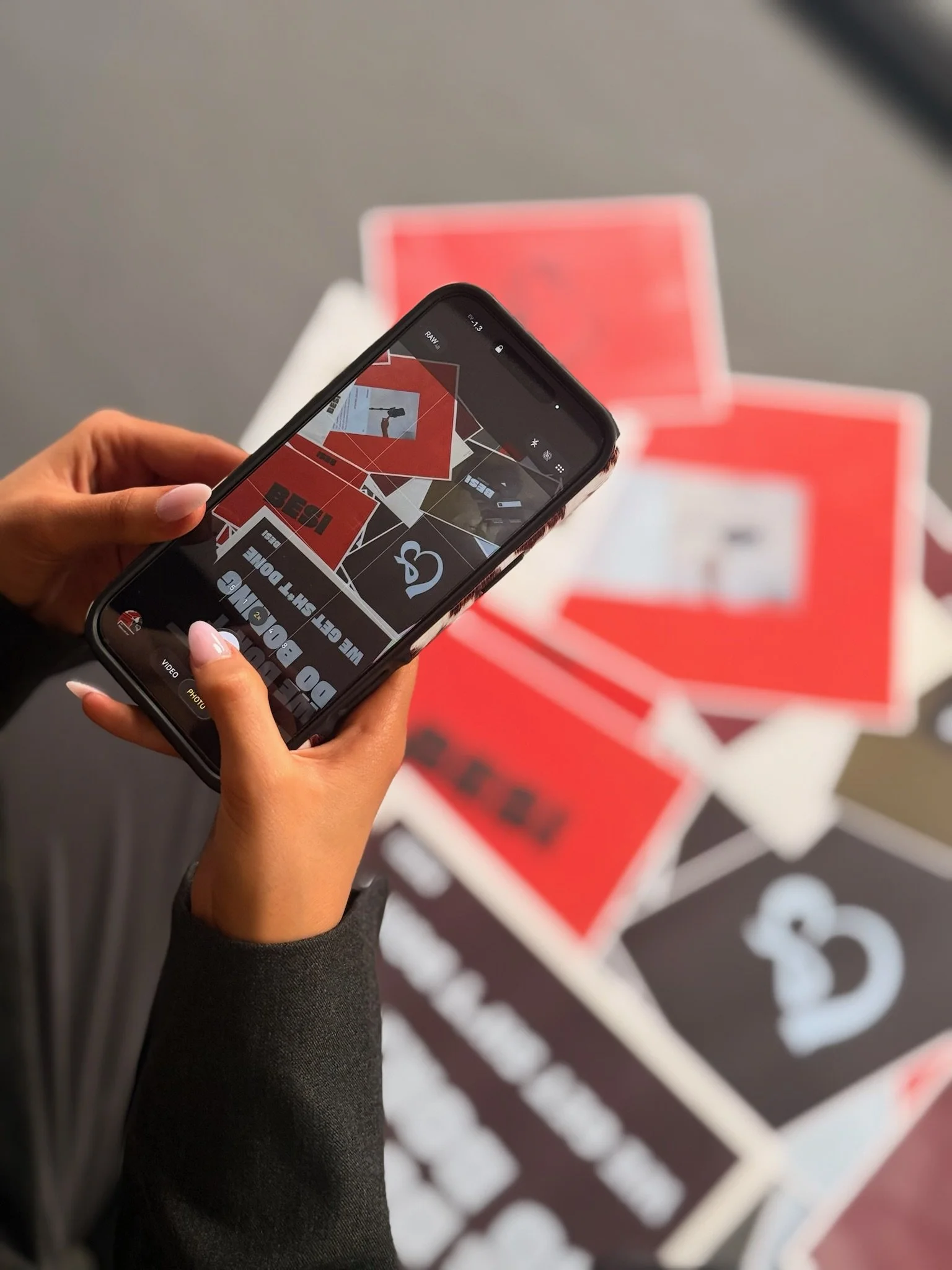 Person taking a photo of red and white printed materials on the floor with a smartphone.