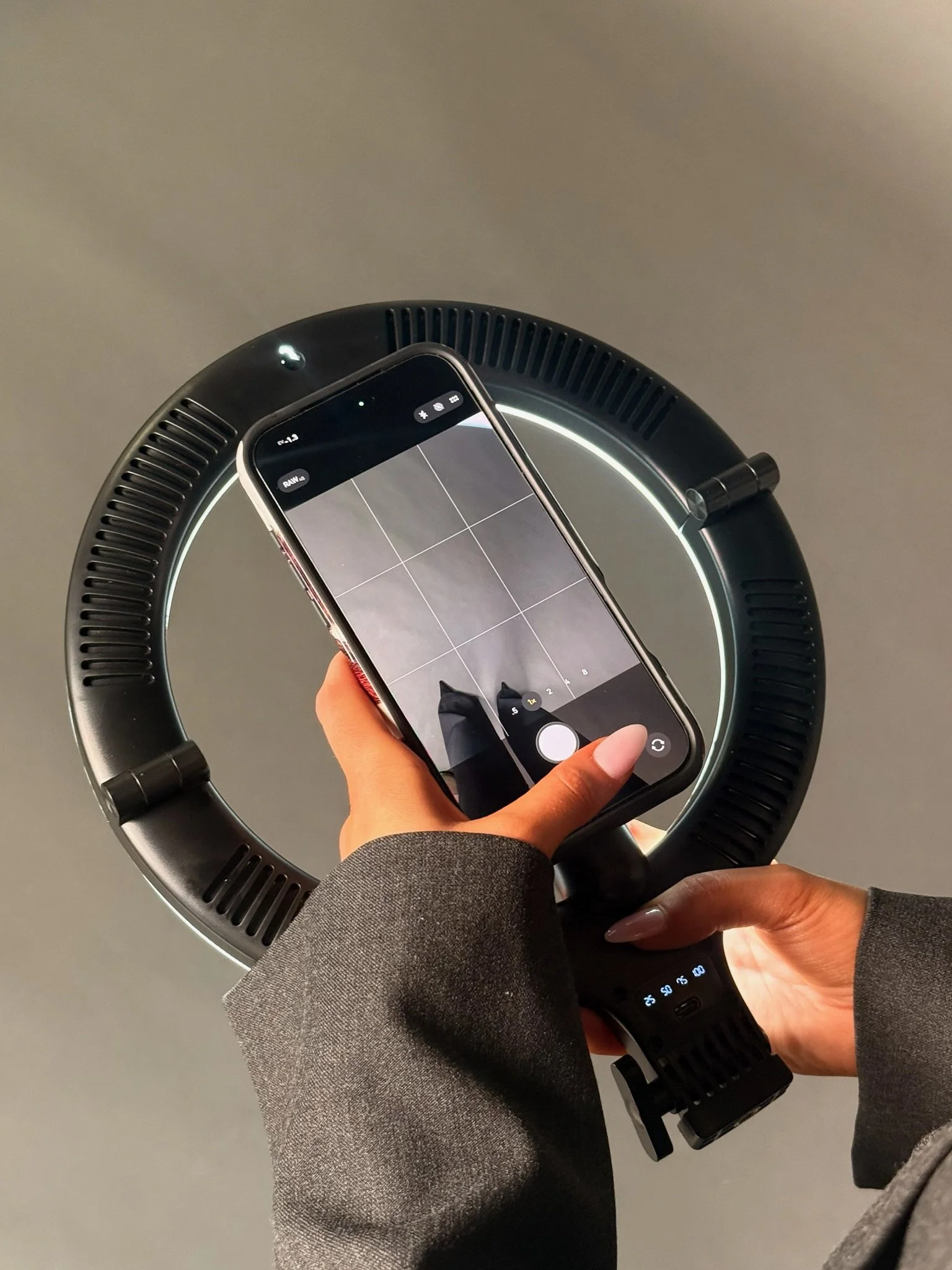 A person's hand holding a smartphone above a circular device with a glowing ring, likely a modern air purifier or similar appliance, on a flat surface.