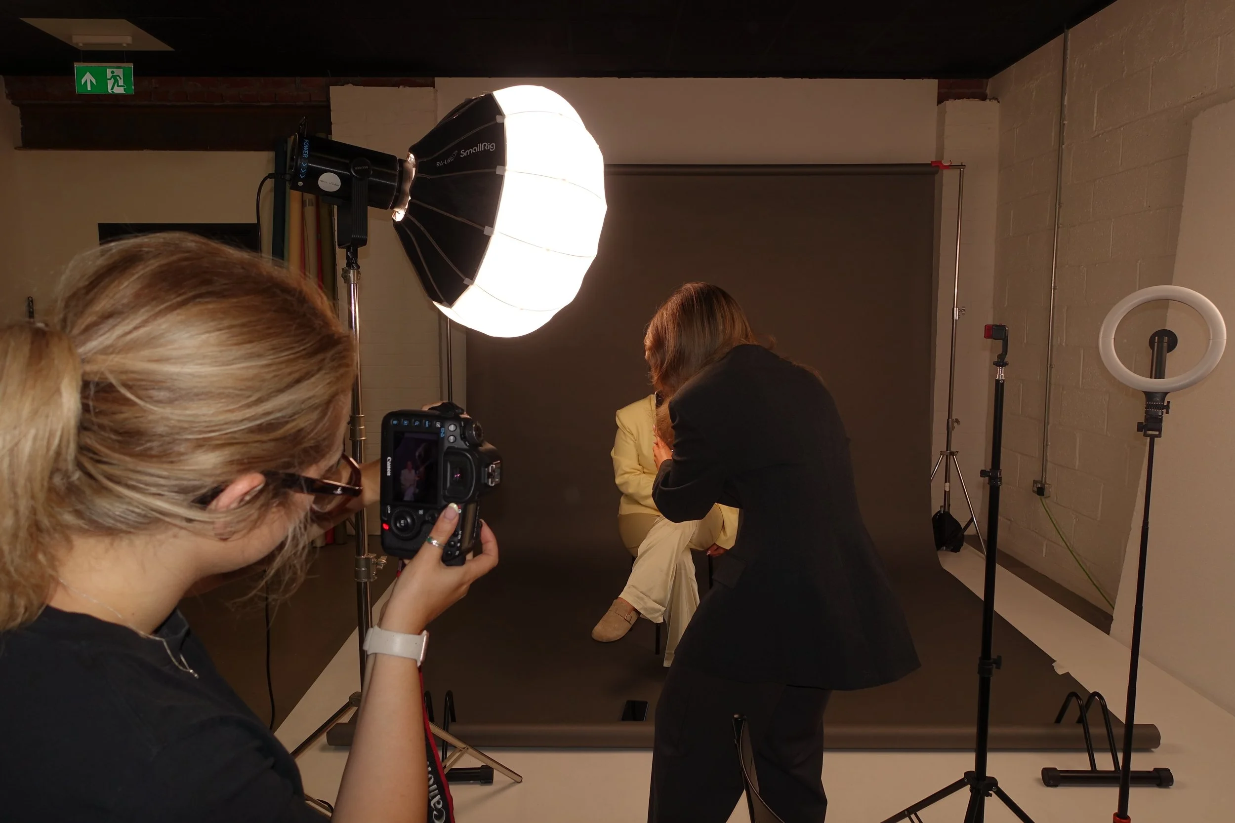 Photographer taking a picture of a woman in a studio with professional lighting equipment for the launch of a marketing agency.