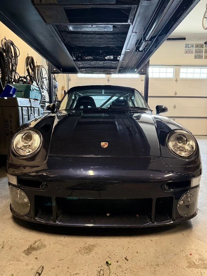 Black Porsche sports car parked in a garage with tools and bicycles on the walls.