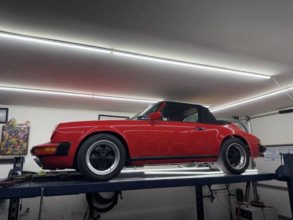 A red classic Porsche 911 sports car on a lift in a garage.