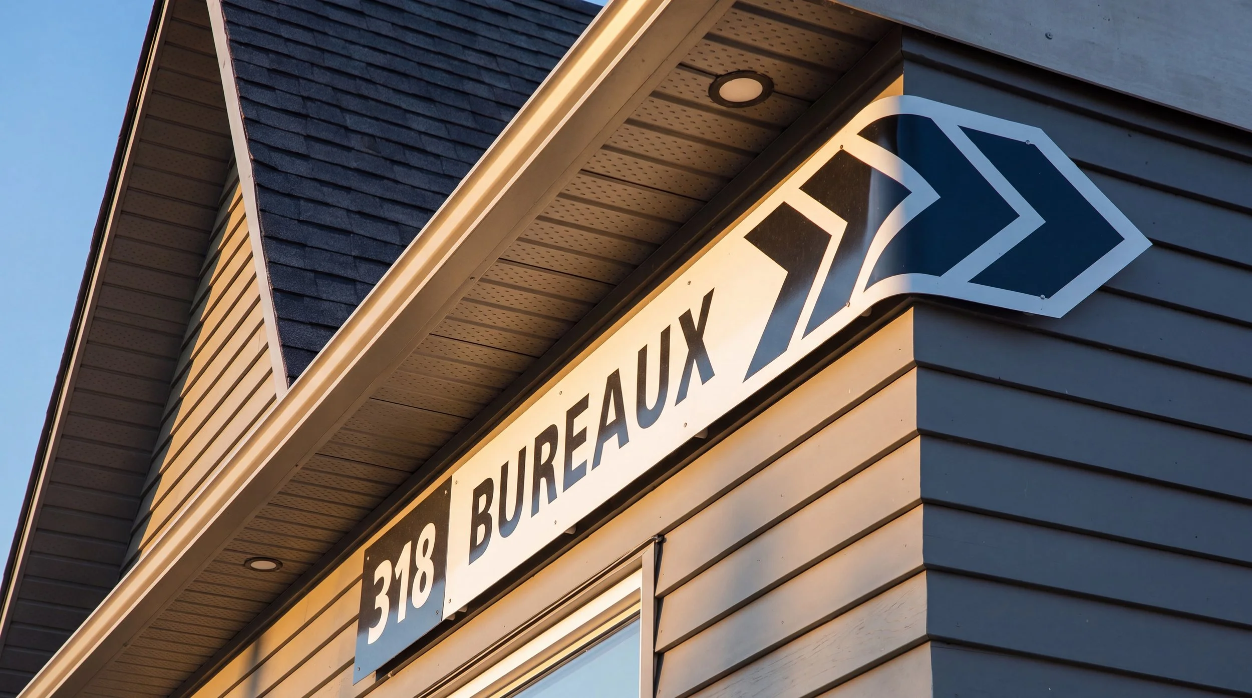 Façade d'un bâtiment avec un panneau indiquant '510 318 BUREAU' et une flèche directionnelle, sous un toit en ardoise.