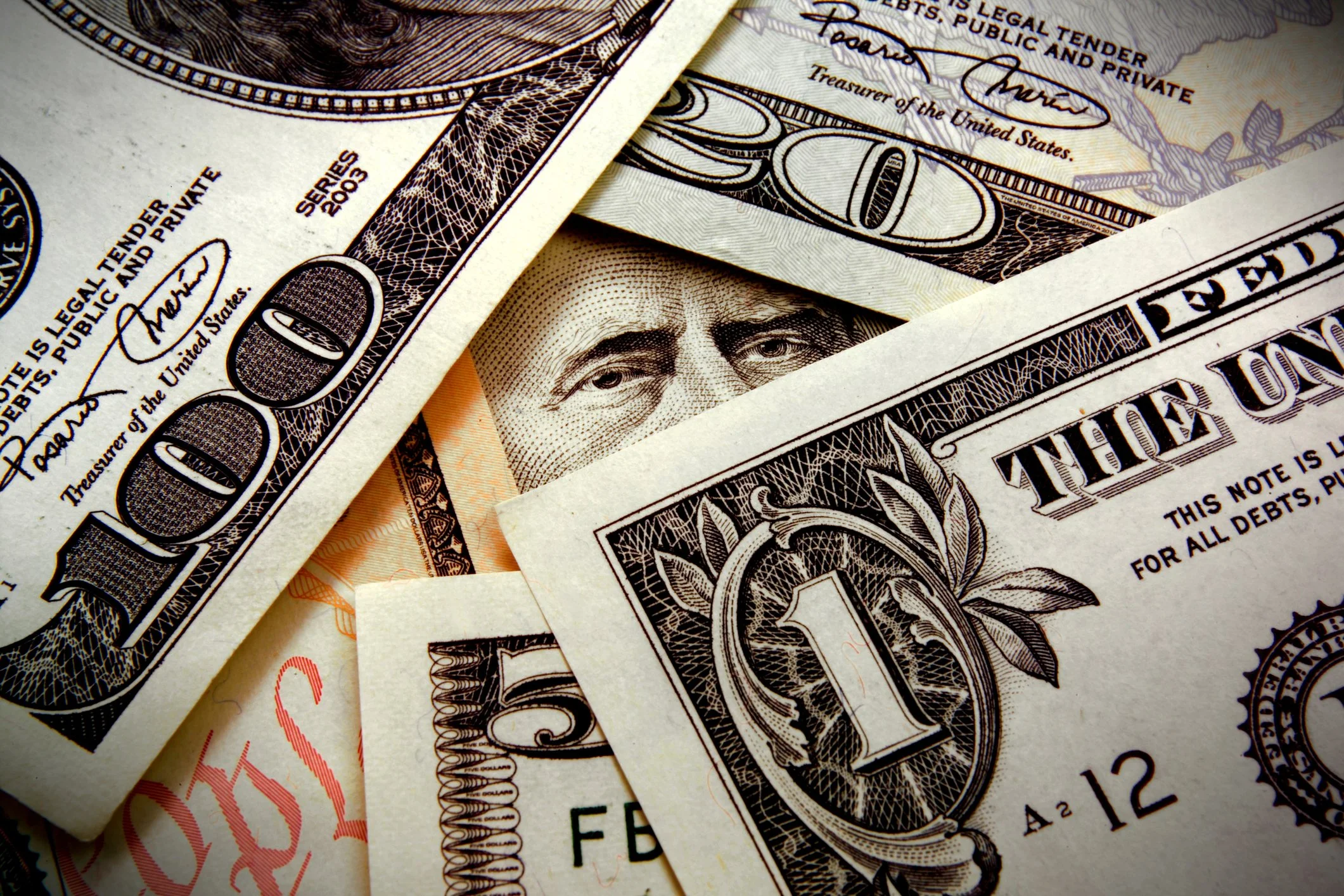 Close-up of multiple overlapping U.S. dollar bills, featuring portraits and intricate designs.