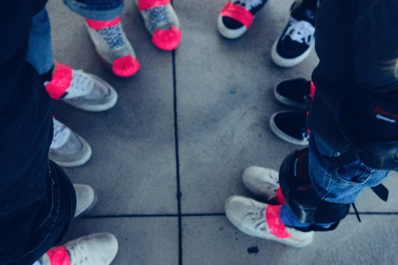 Top-down view of people standing in a circle, showing only their feet and shoes on a tiled floor.
