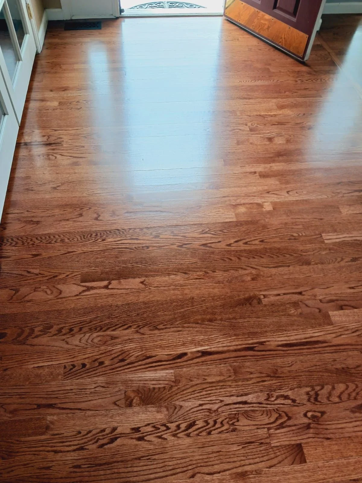 Close-up view of a shiny hardwood floor near an open door, with part of a wooden cabinet visible on the right.