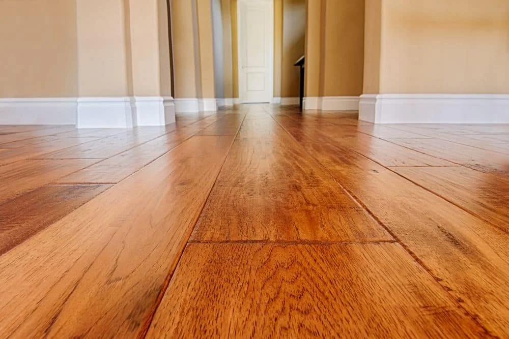 Close-up view of a wooden floor with a hallway and white door at the end in a house interior.