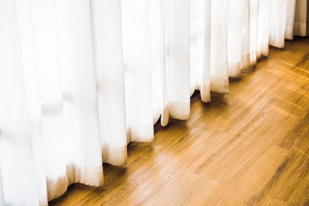 White curtains hanging near a wooden floor.