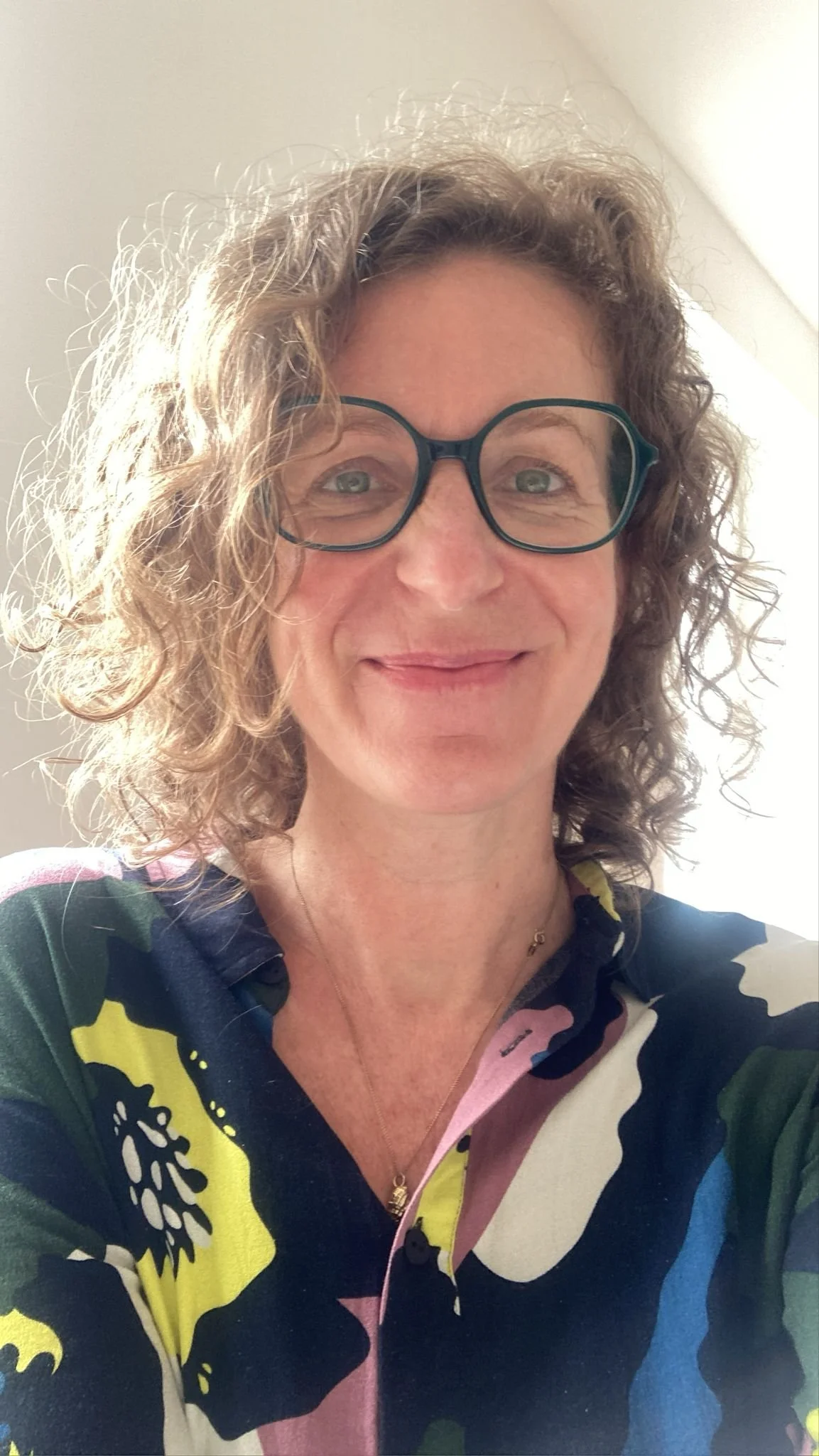 Portrait einer lachenden Frau mit Locken und einer Bluse mit buntem Muster