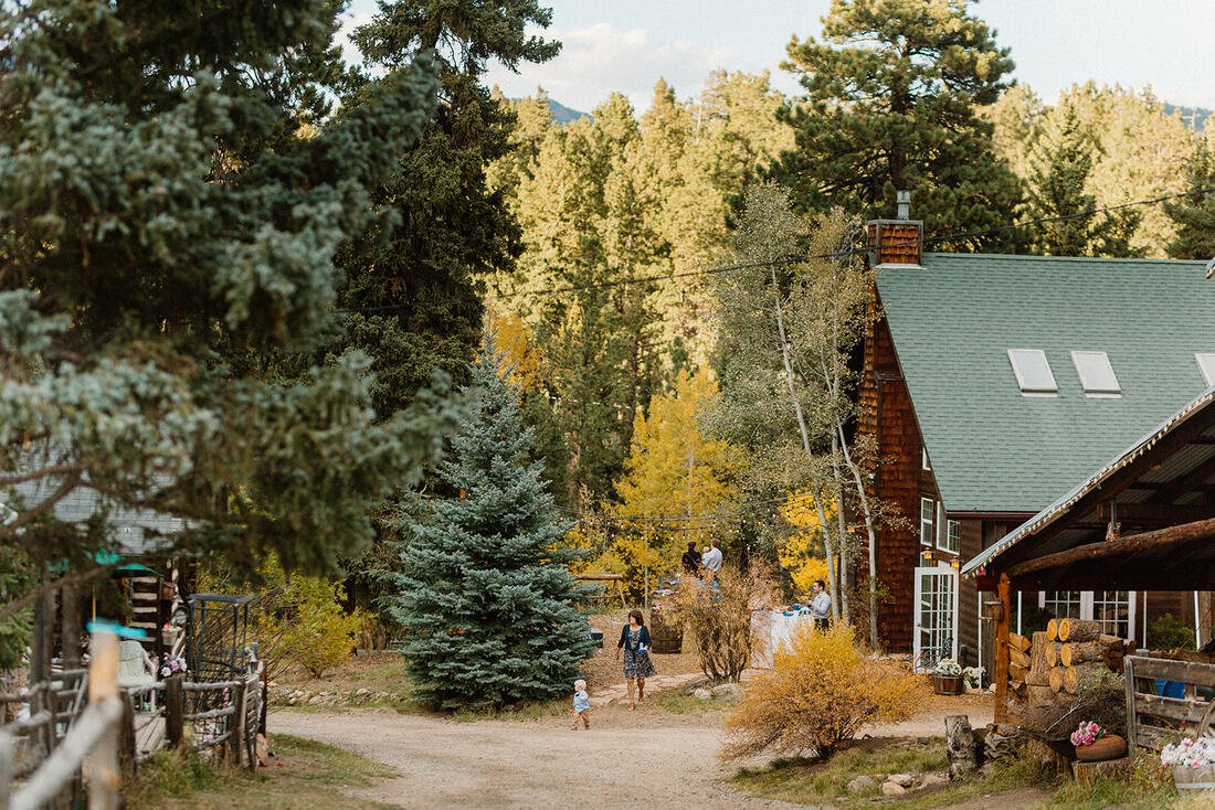 Meadow Creek event center with people socializing surrounded by trees, under a partly cloudy sky.