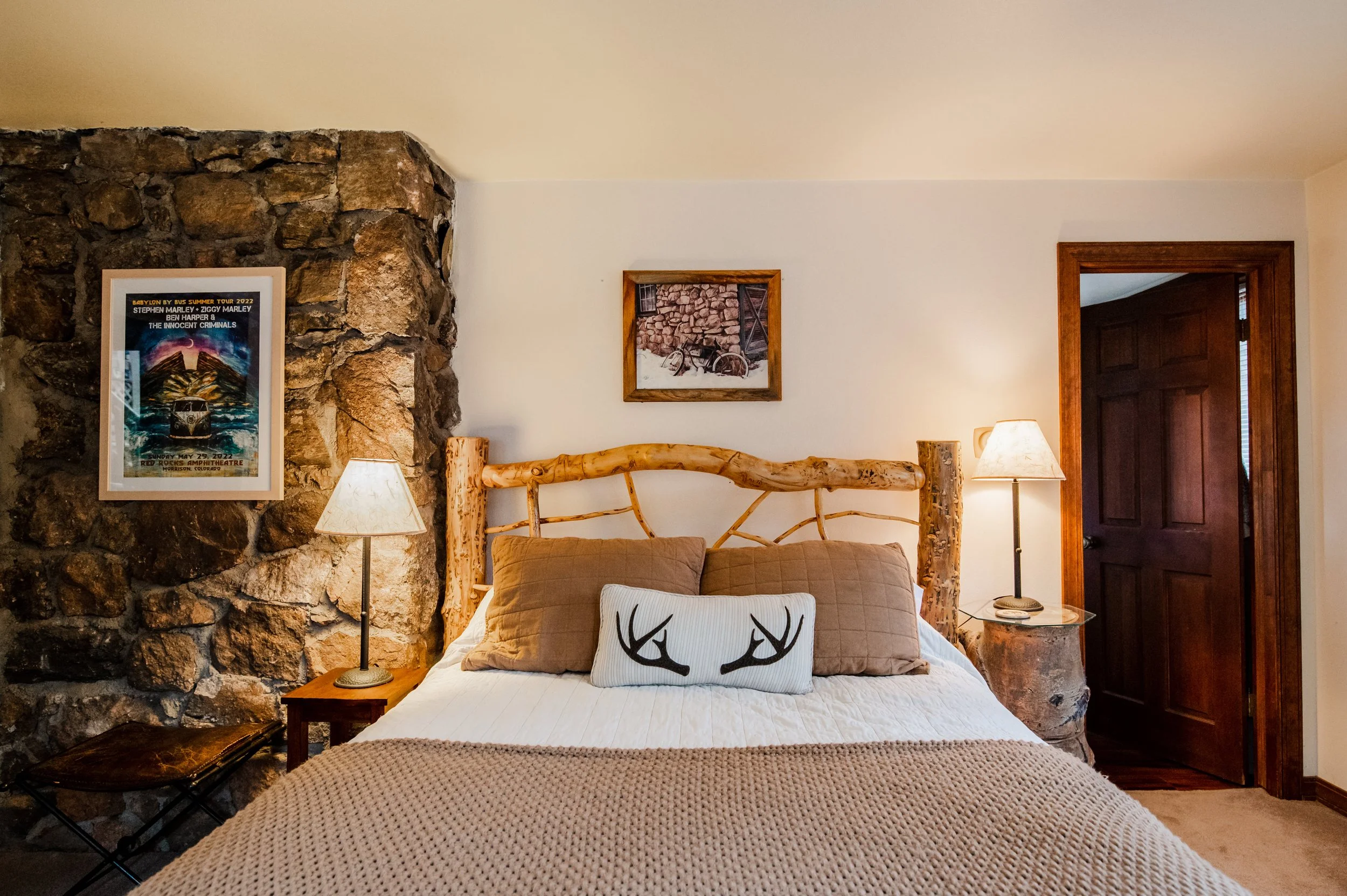 A cozy bedroom with a rustic log bed, decorative pillows, and a stone wall with framed artwork.