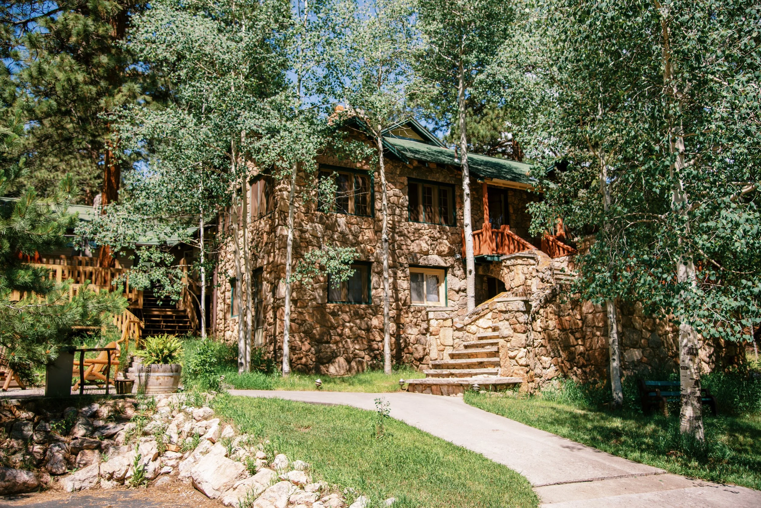 Meadow Creek Lodge surrounded by tall green trees with a stone staircase leading to the entrance and a curved concrete pathway in front.