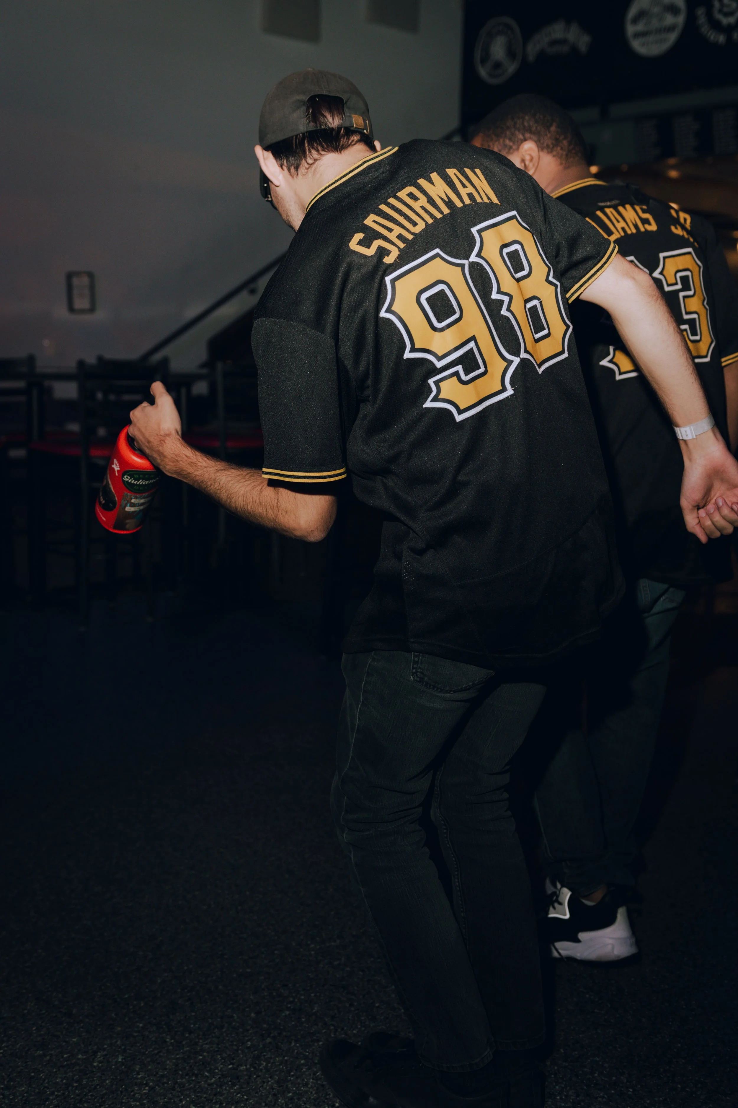 Bill Saurman and Dwayne Williams Jr of Perpetual Motion wear black jerseys with yellow and white names and numbers, one reading 'Saurman 90' and the other 'Williams 23', are standing in a dark indoor setting.