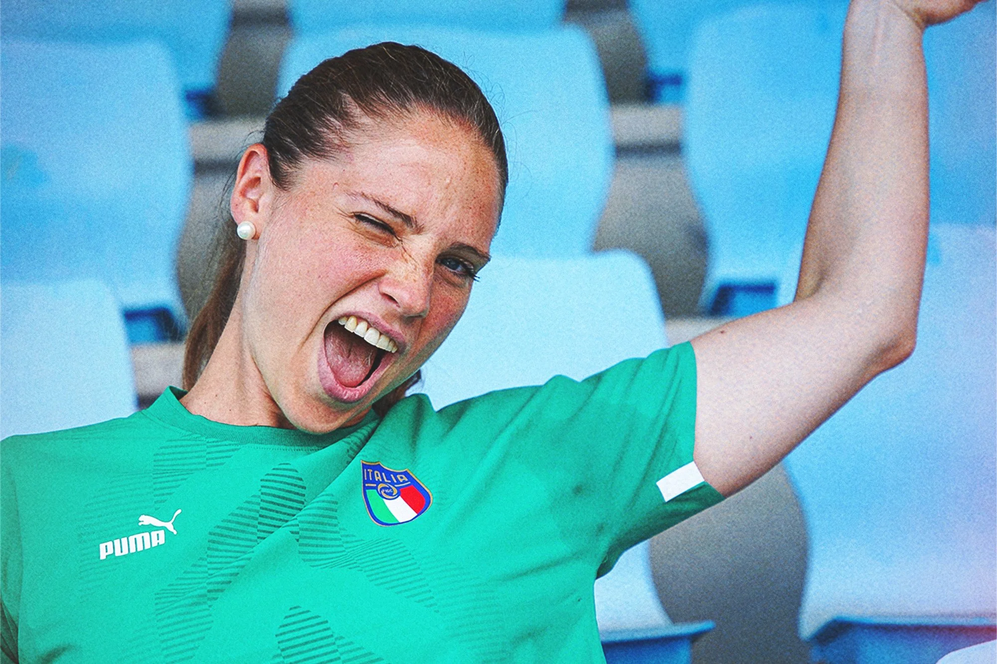 Donna che celebra, indossa una maglia verde con il logo dell'Italia sul petto e segnala un successo con la mano.