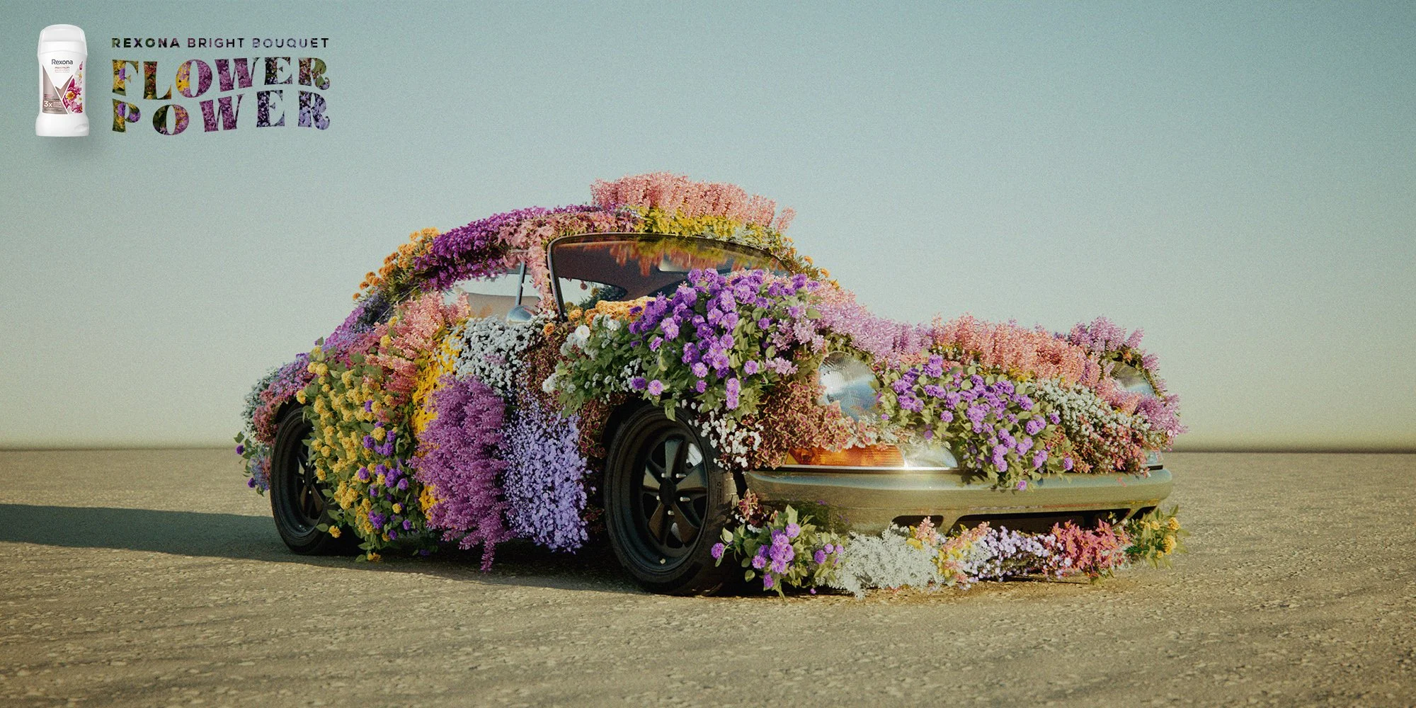 Auto ricoperto di fiori di vari colori, tra cui lilla, rosa, bianco e giallo, posizionato su una superficie di asfalto. In alto a sinistra, c'è un logo di un deodorante Rexona e il testo 'Rexona Bright Bouquet Flower Power' scritto con lettere decorate da motivi floreali.