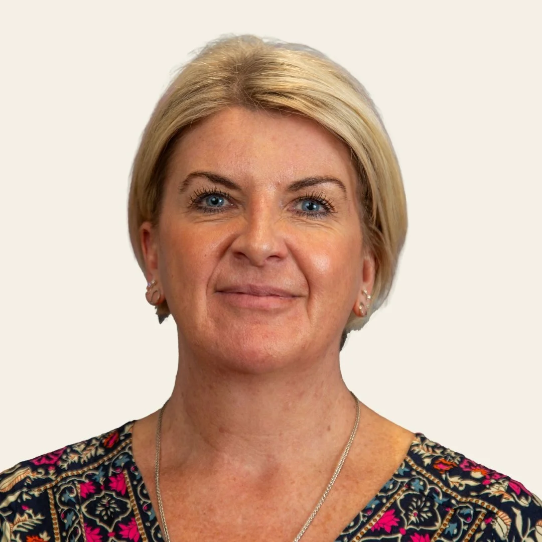 close-up of a woman with short blonde hair, blue eyes, and wearing a patterned top.