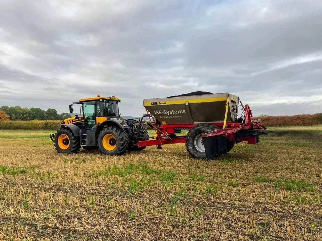 A tractor with a seed spreader attachment working in a field under cloudy skies.