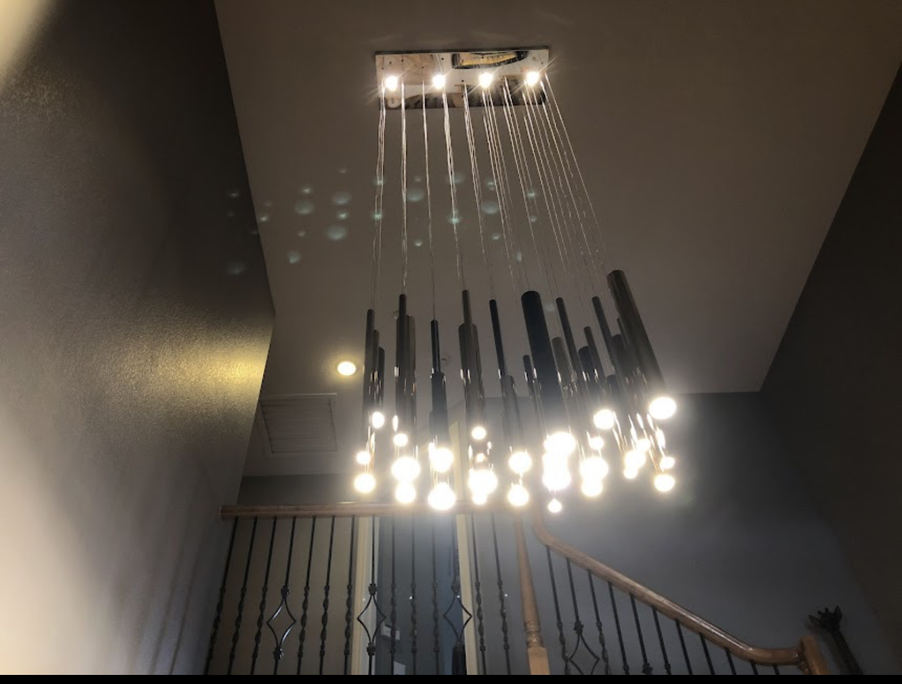 Modern chandelier with multiple hanging lights installed on a ceiling above a staircase.