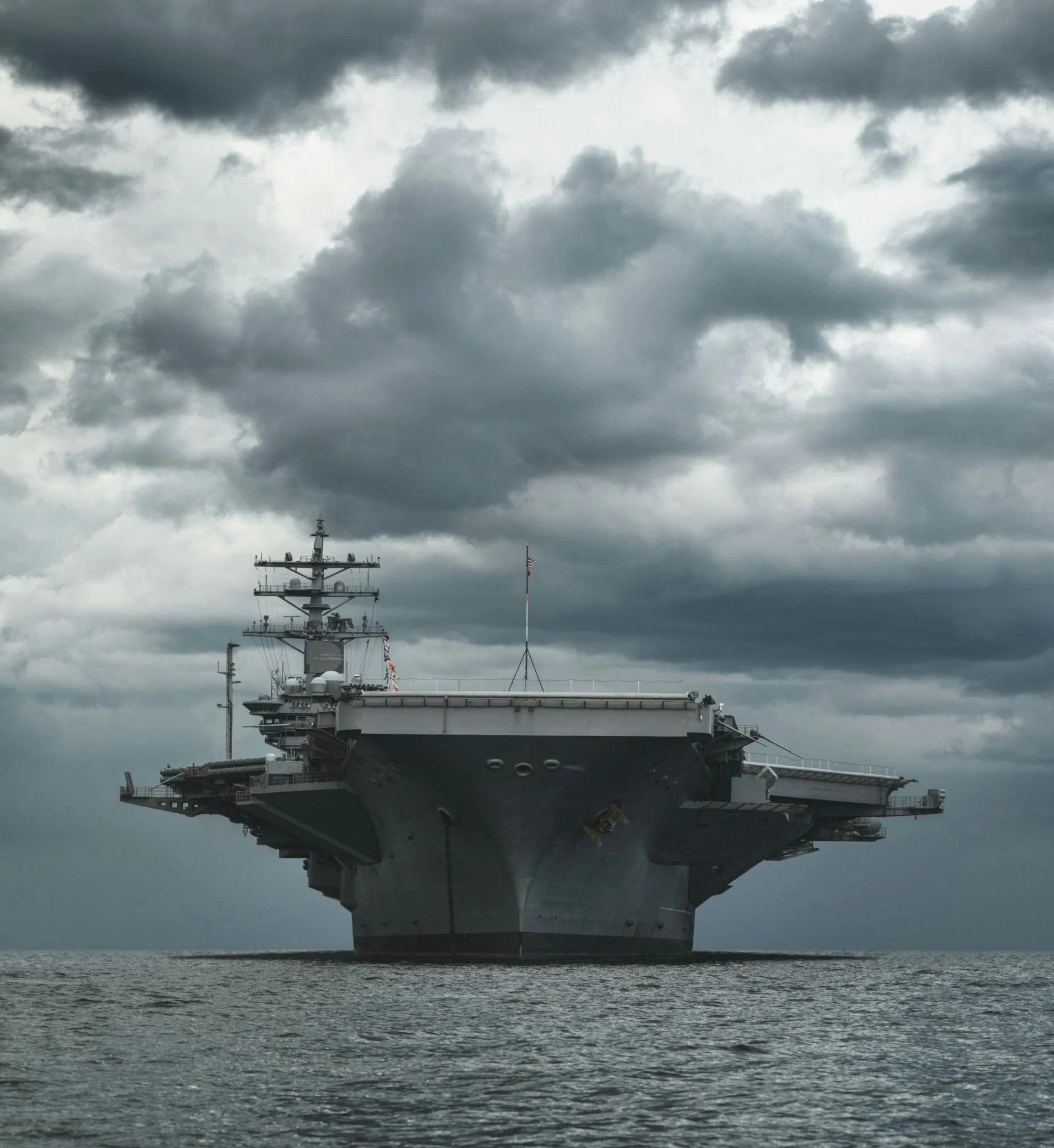 A large aircraft carrier at sea with a cloudy sky overhead.