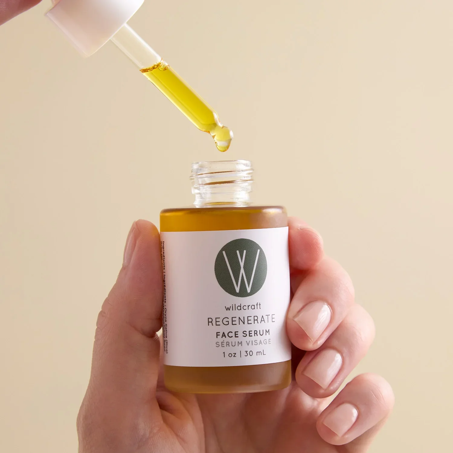 A hand holding a bottle of Wildcraft Rejuvenate Face Serum with a dropper releasing serum into the bottle
