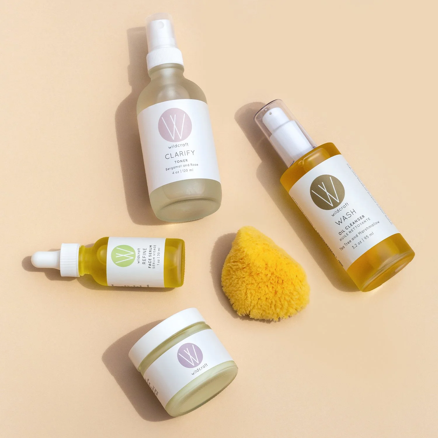 A collection of Wildcraft skincare products, including a toner, a face serum, a wash, and a small container, along with a yellow sponge on a beige background.