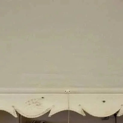 Close-up of a white surface with some dark spots and a string hanging from the top, with a scalloped edge at the bottom. This roller blind was then reversed and a new scallop put back on