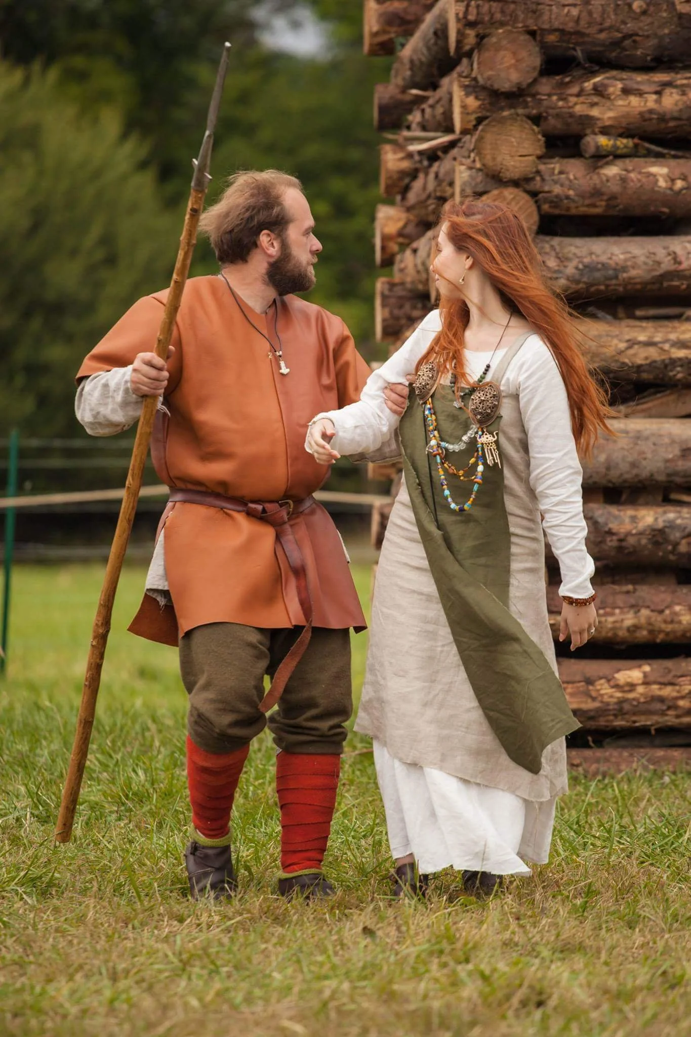 Un homme et une femme en costume médiéval se tenant la main dans un champ, avec un tas de bois derrière eux.