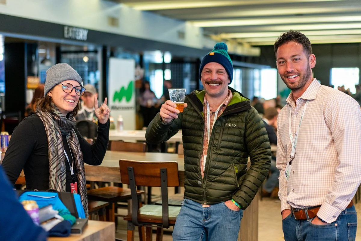 manufacturing networking events. Three people smiling and socializing at a bar or restaurant, with one holding a drink, in a lively indoor setting.