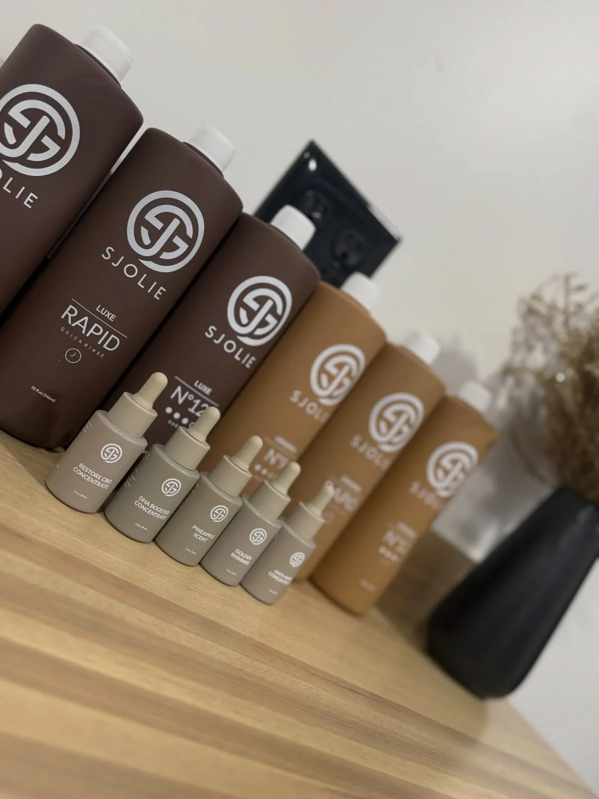 Collection of SJOLIE skincare products including bottles and droppers on a wooden surface.